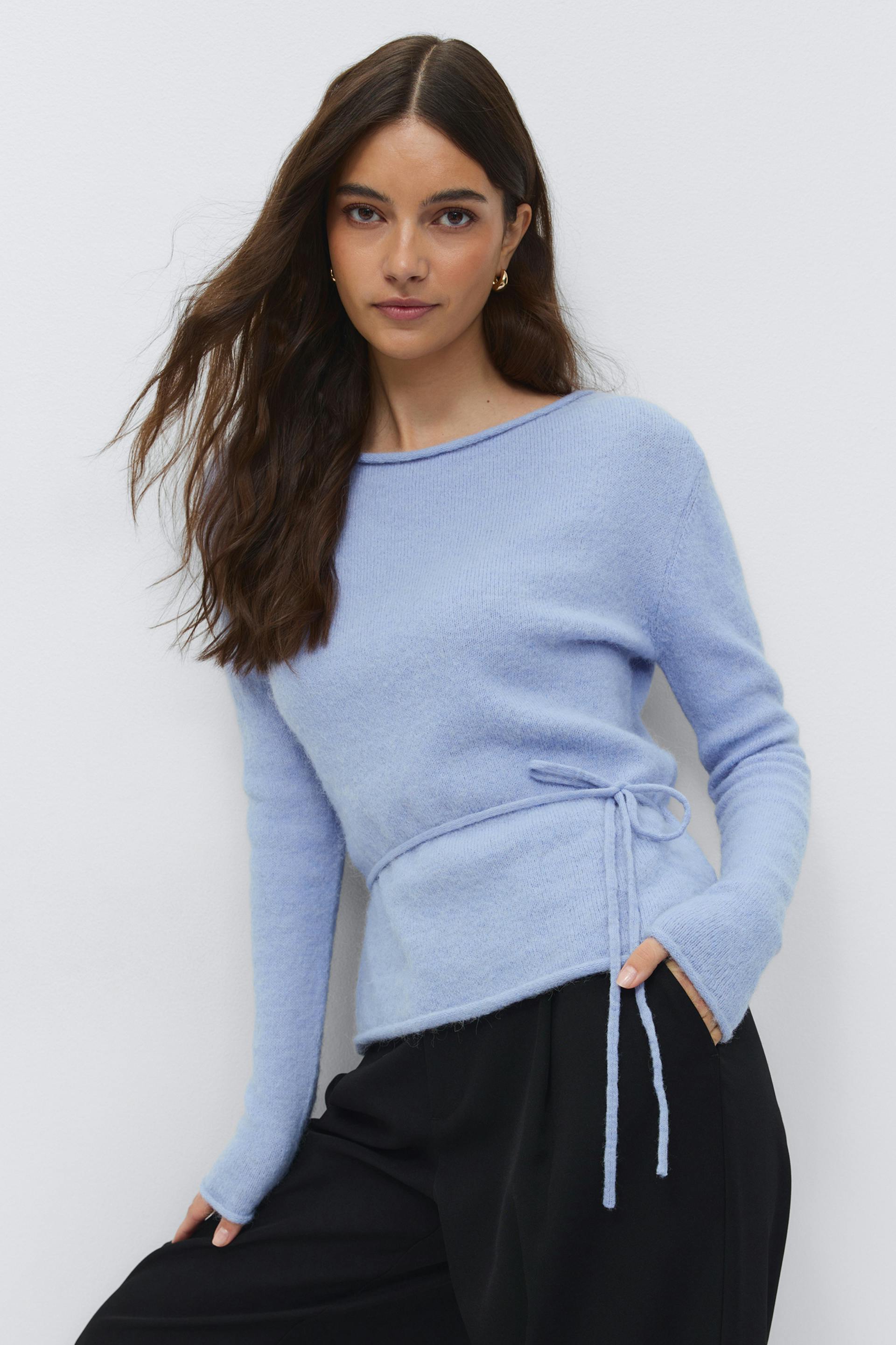 Light blue fuzzy knit long-sleeve sweater with a boat neckline and thin self-tie waist belt, paired with black wide-leg trousers.