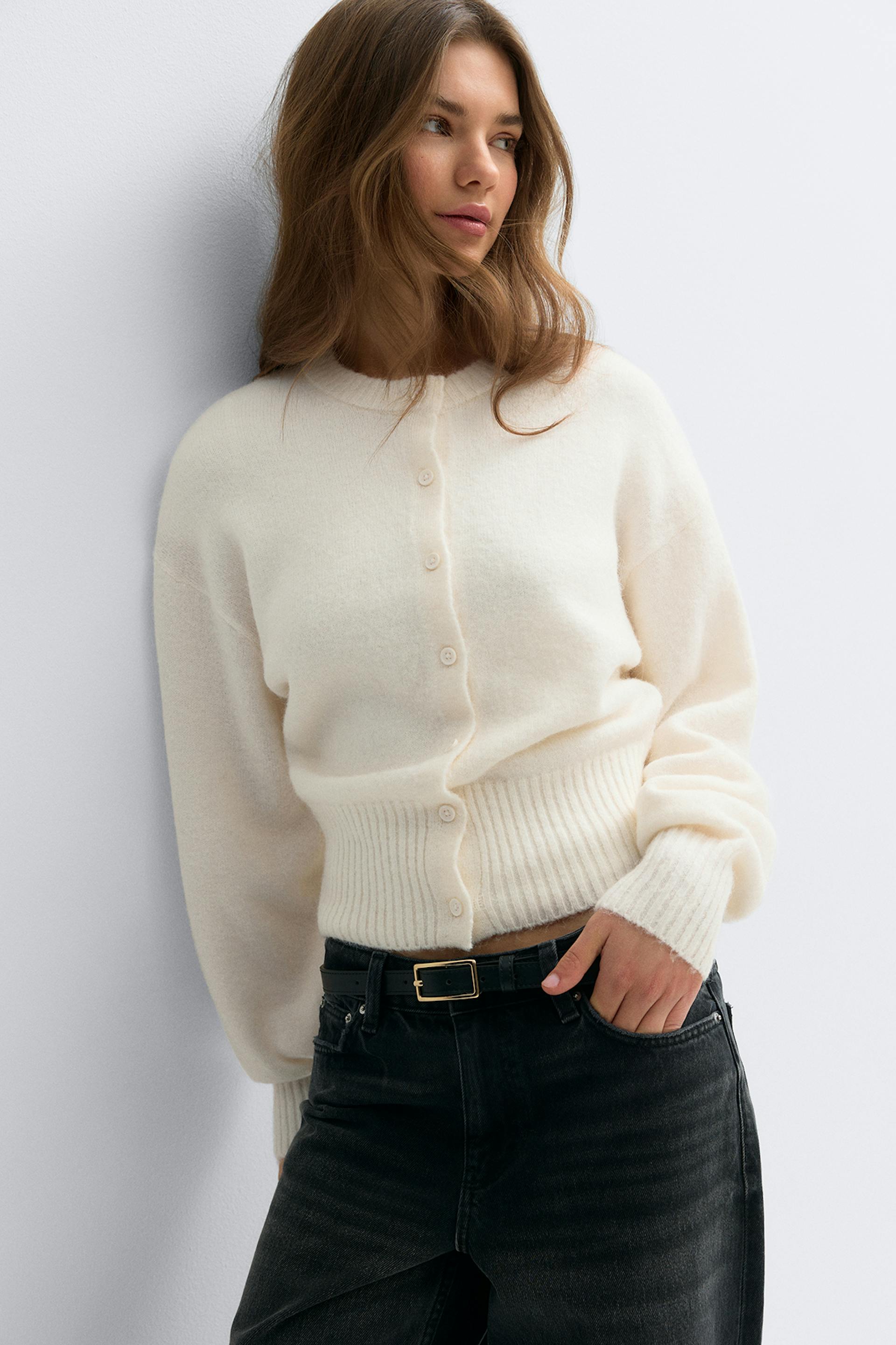 Kermanvärinen, napitettu, napitettava, kauluksellinen neuletakki, jossa on uurrettu helma ja hihansuut, yhdistettynä korkeavyötäröisiin mustiin farkkuihin ja mustaan vyöhön, jossa on kullanvärinen suorakulmainen solki.