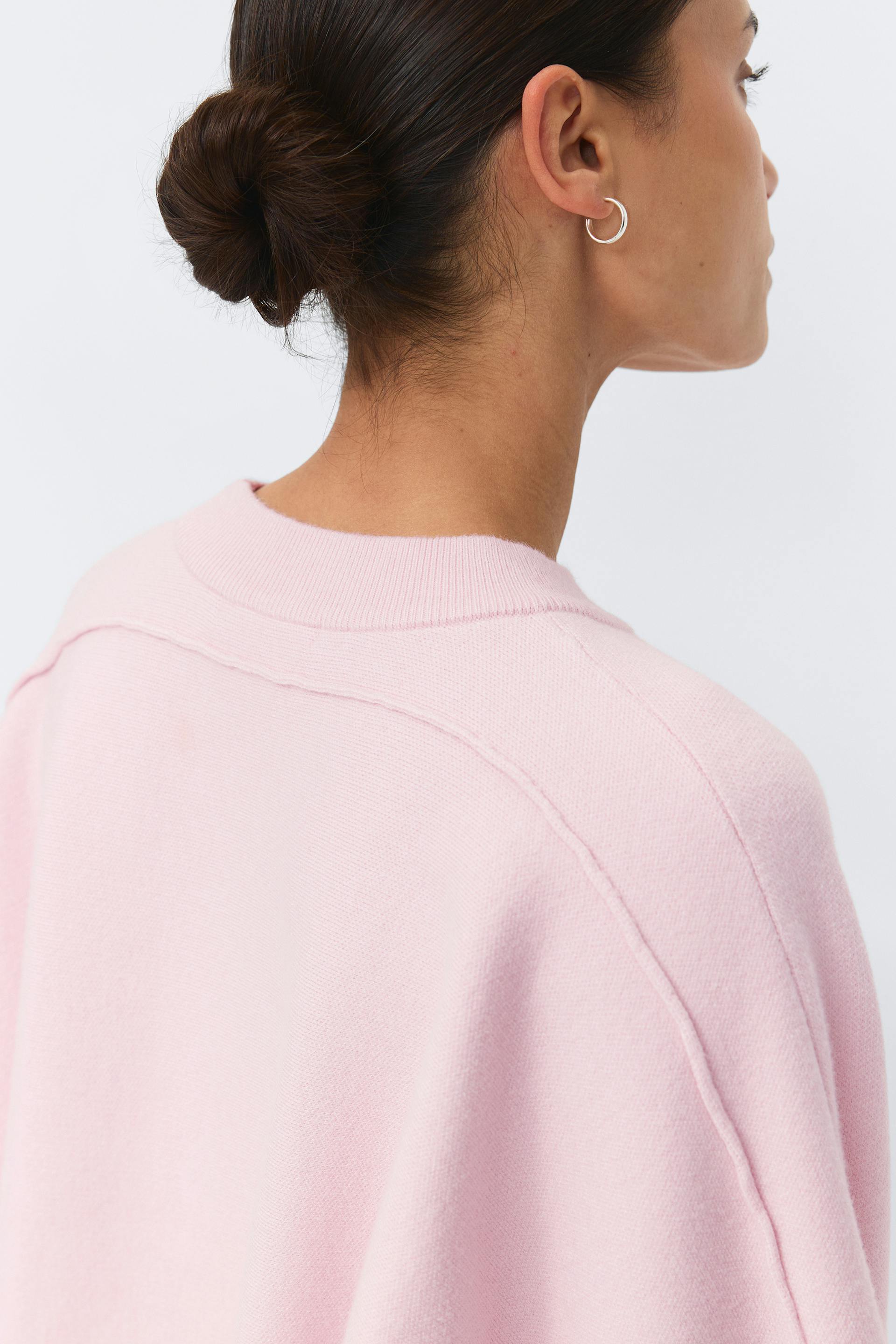 Vaaleanpunainen pusero, jossa on pudotetut olkapäät ja näkyvät saumakohdat, yhdistettynä pieniin hopeisiin korvakoruihin.