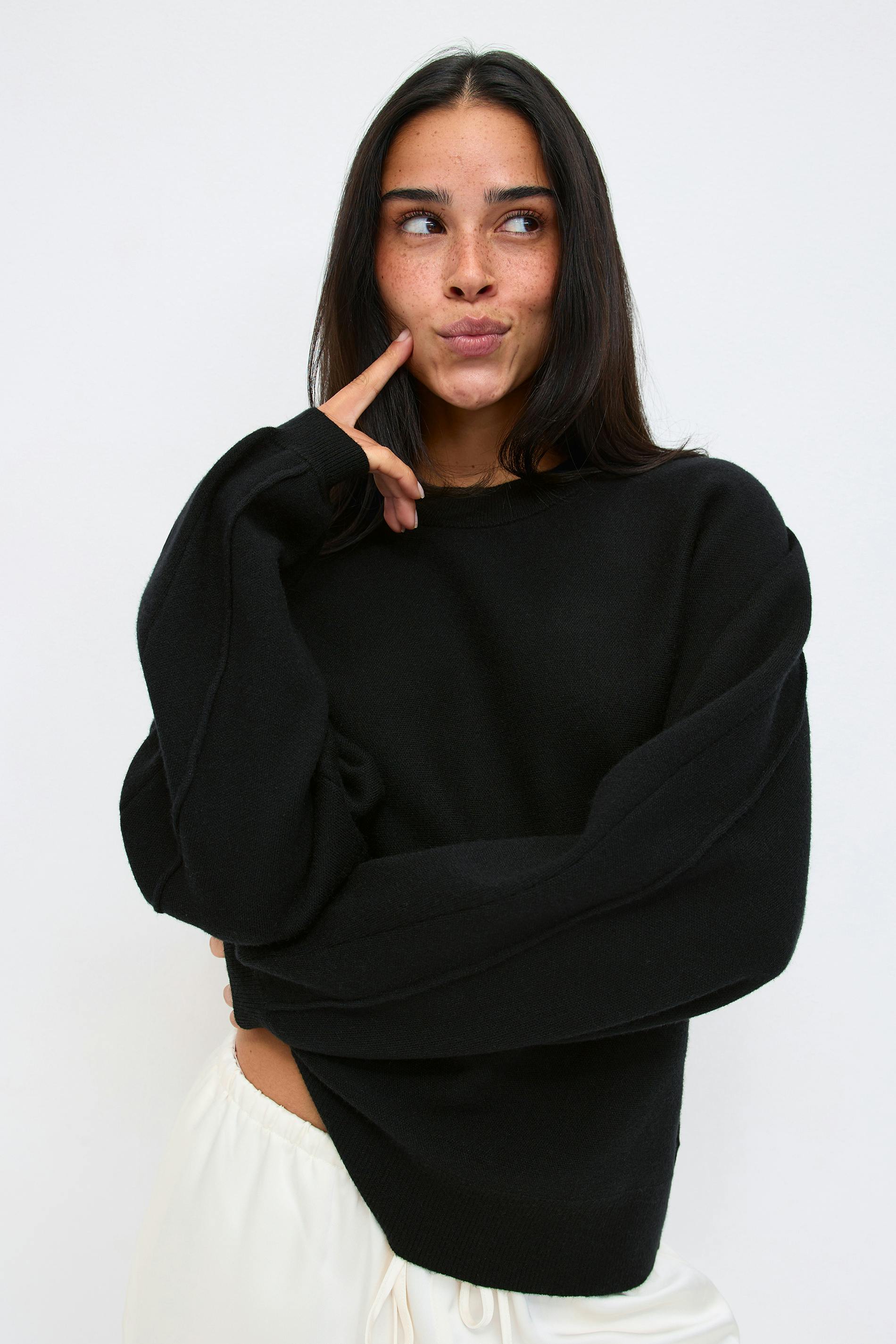 Black oversized crew-neck knit sweater with ribbed cuffs and hem, paired with white drawstring-waist trousers.