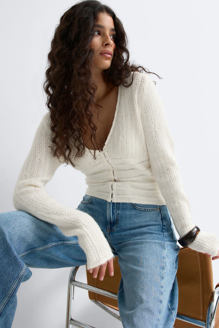 Cremefarbene Strickjacke mit Knopfleiste und langen Ärmeln aus Rippenstrick, kombiniert mit hellblauen Jeans mit hoher Taille.