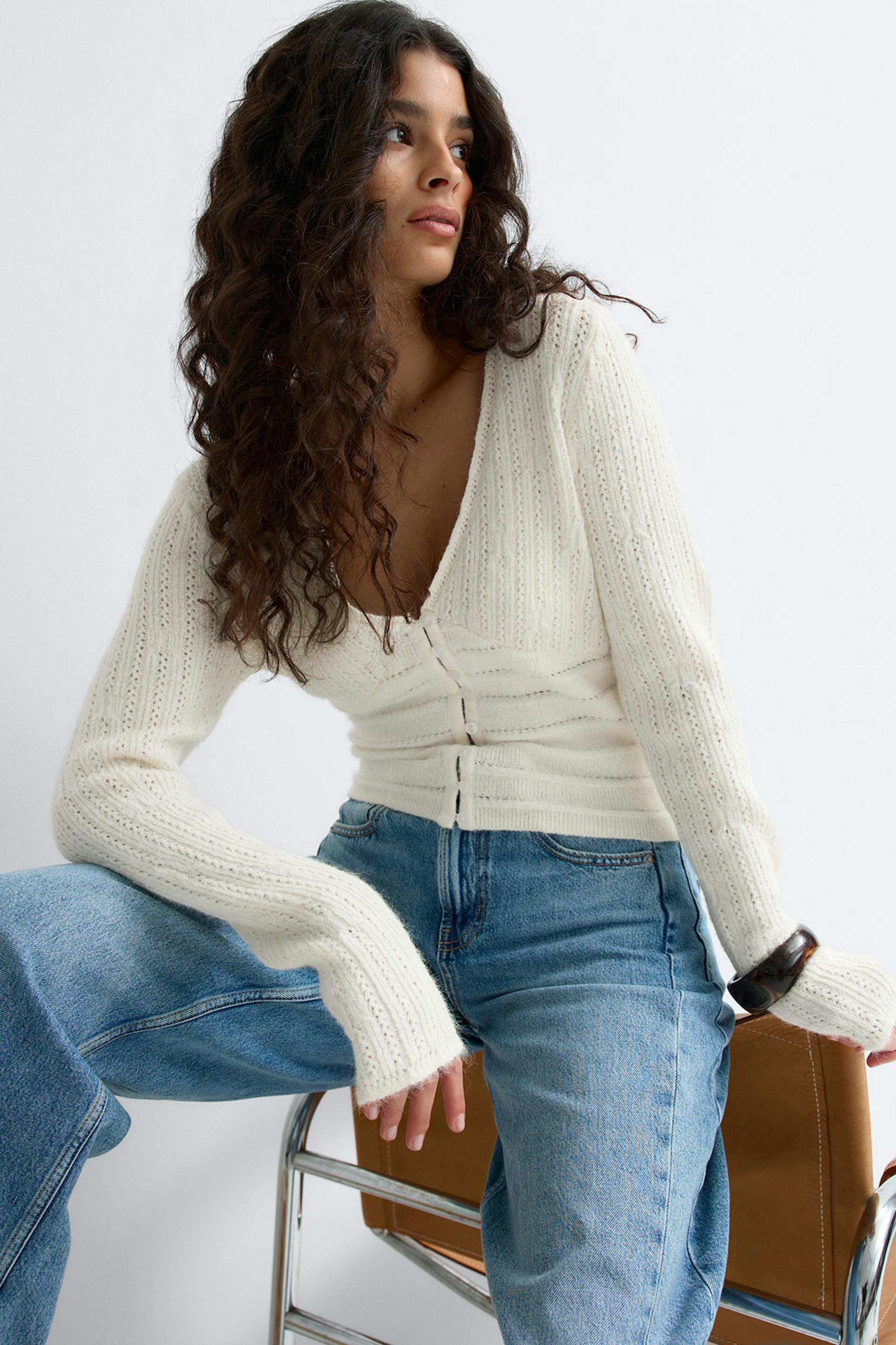 Kermanvärinen, pitkähihainen, nappineulottu neuletakki, jossa on pitkät hihat, yhdistettynä vaaleansinisiin korkeavyötäröisiin farkkuihin.