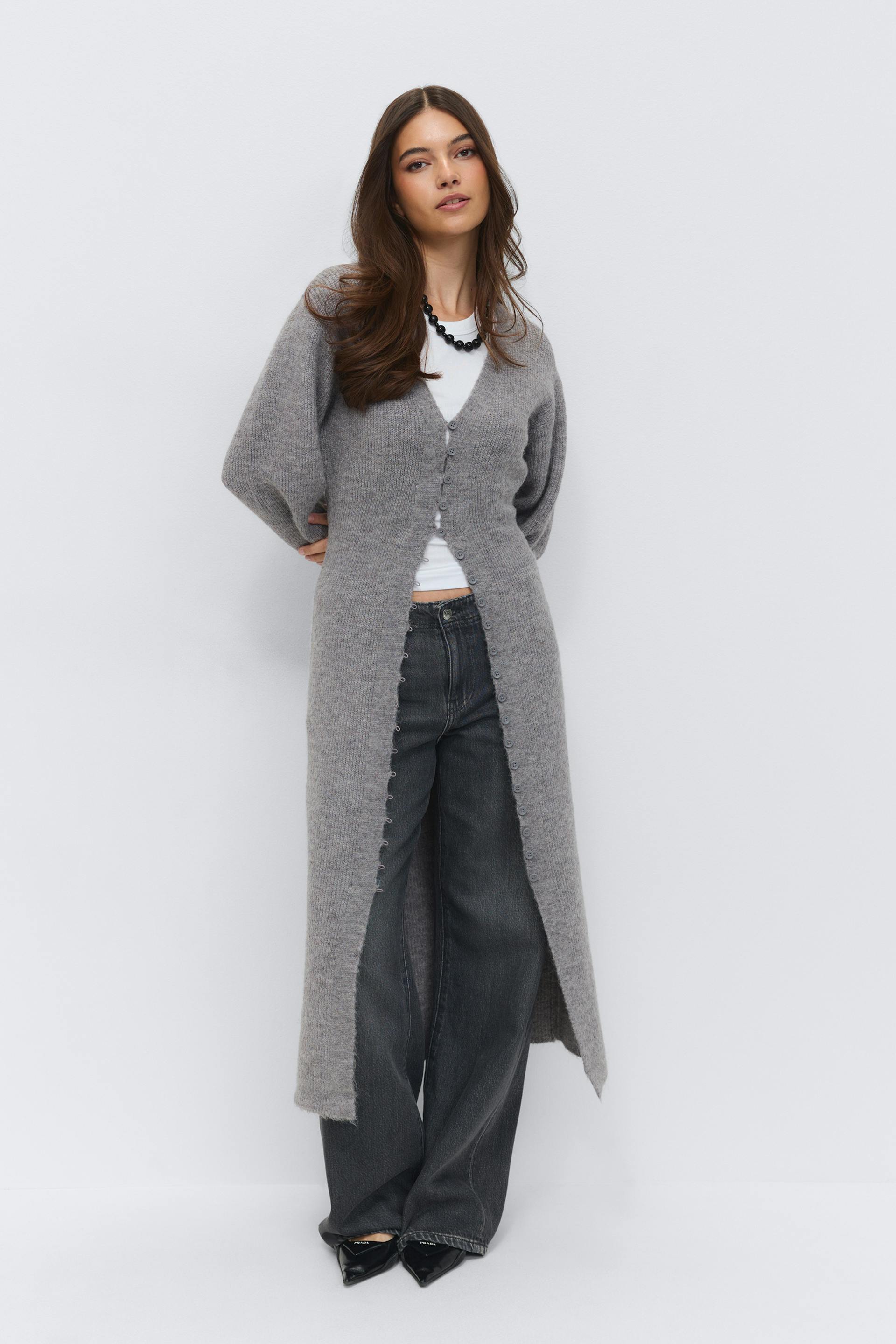 Grey long button-front knitted cardigan over a white crew-neck T‑shirt, paired with dark wide-leg jeans, black pointed-toe heels and a black beaded necklace.