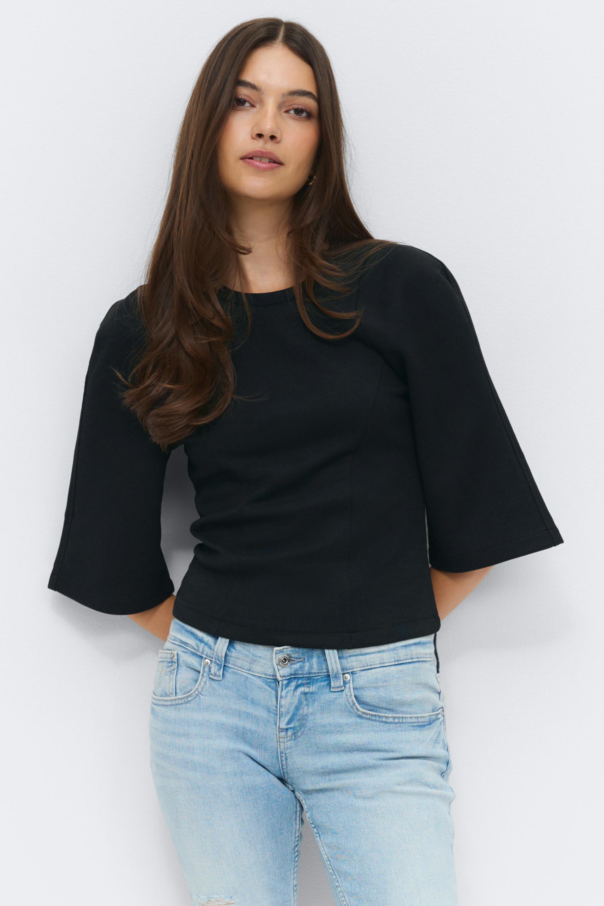 Black fitted top with crew neckline and elbow-length flared sleeves, paired with light-wash slim jeans with subtle distressing.