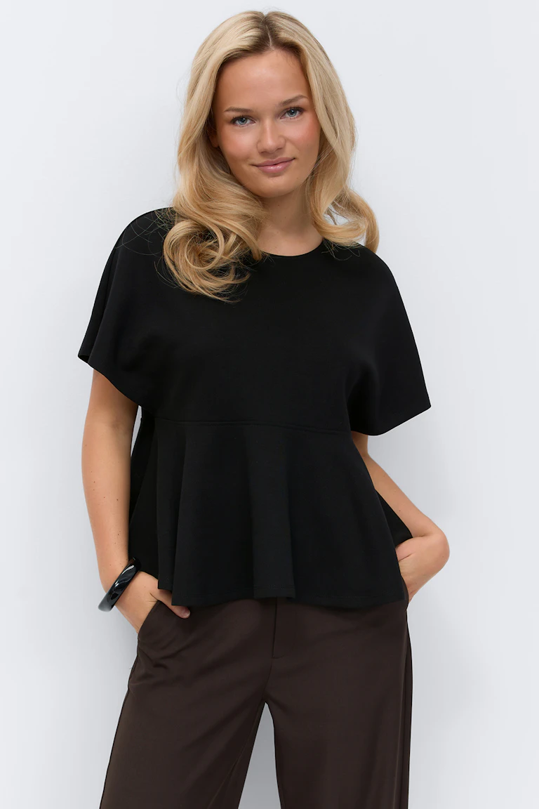 Black short-sleeve peplum top with round neckline, styled with dark brown tailored trousers and a black cuff bracelet.