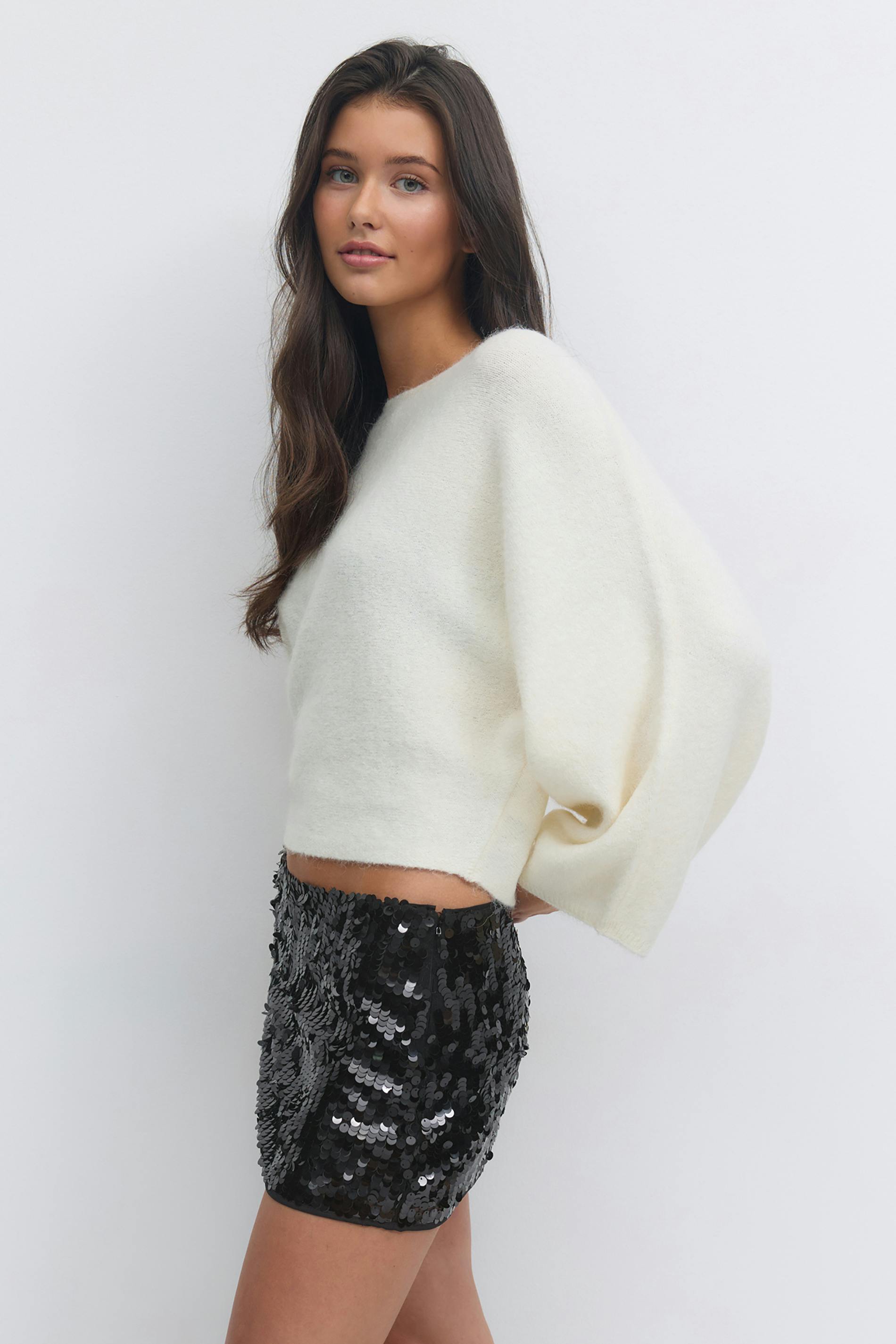 Cropped cream fuzzy sweater with voluminous sleeves, paired with a black sequin mini skirt.