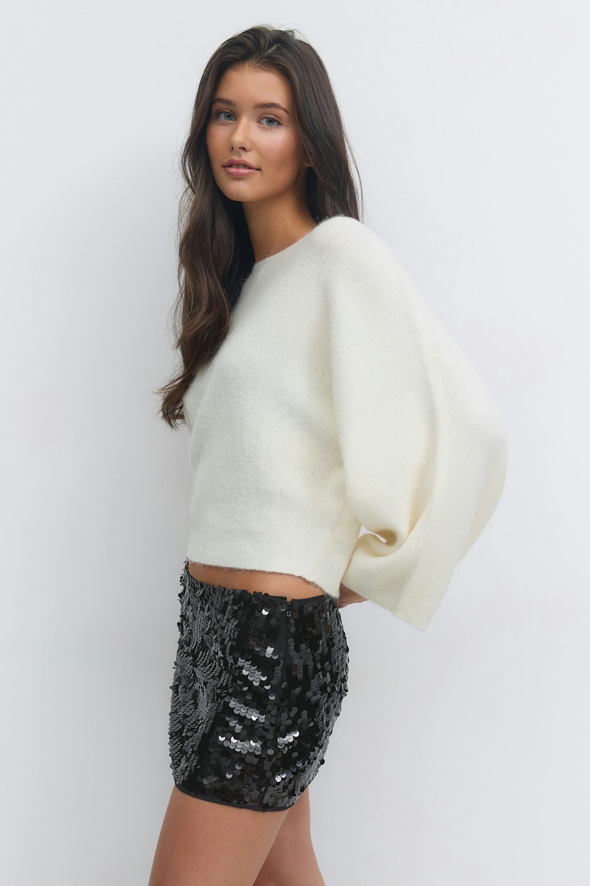 Cropped cream fuzzy sweater with voluminous sleeves, paired with a black sequin mini skirt.