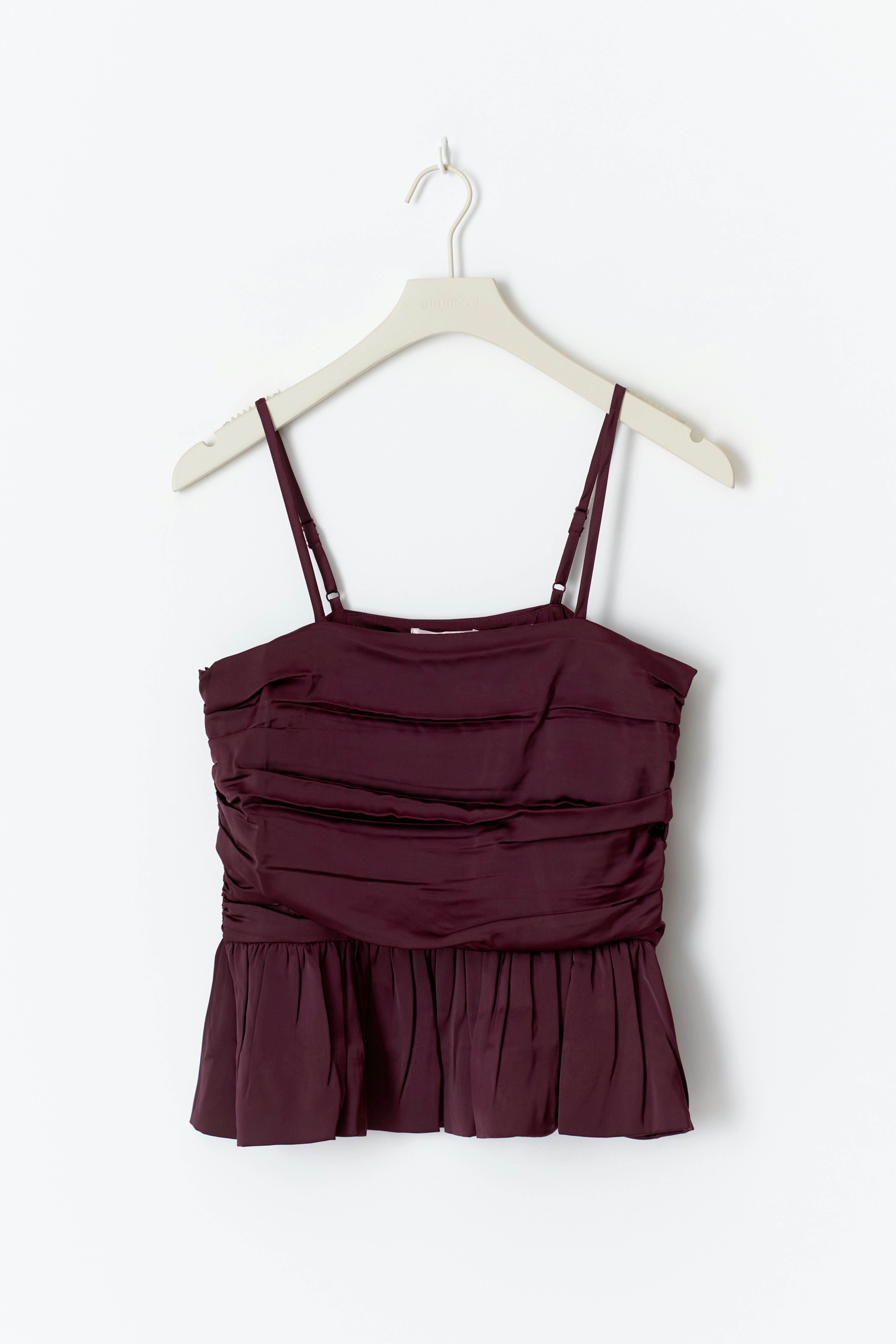 Tief burgunderrotes Spaghettiträger-Oberteil aus Satin mit Schößchen, kombiniert mit hellen Jeans, silbernen Reif-Ohrringen, einem klobigen silbernen Manschettenarmband und mehreren silbernen Ringen.