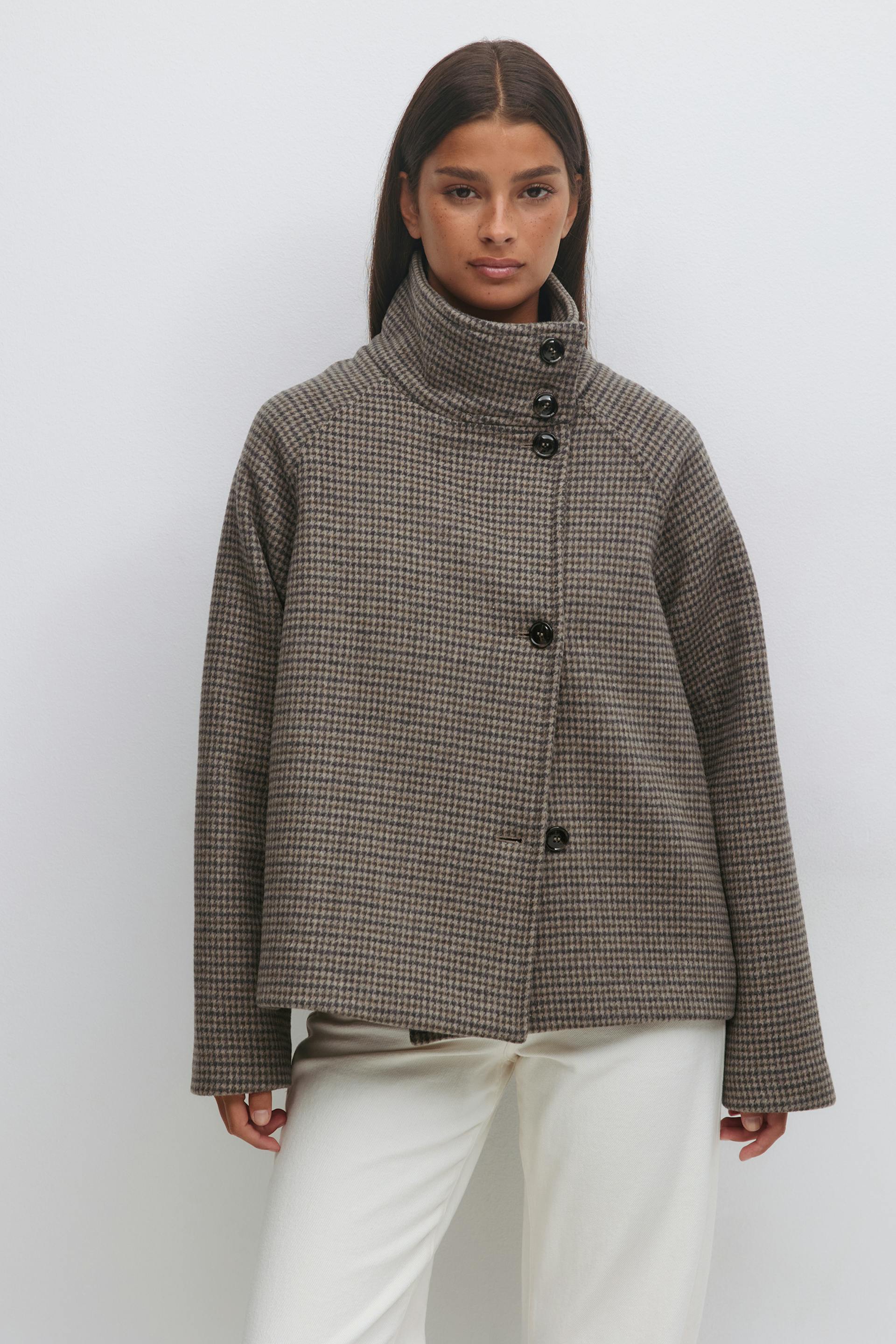 Dubbelknäppt croppad ullrock med hög hals i brun mikrohoundstooth med svarta knappar och långa ärmar, kombinerad med benvita byxor med raka ben.