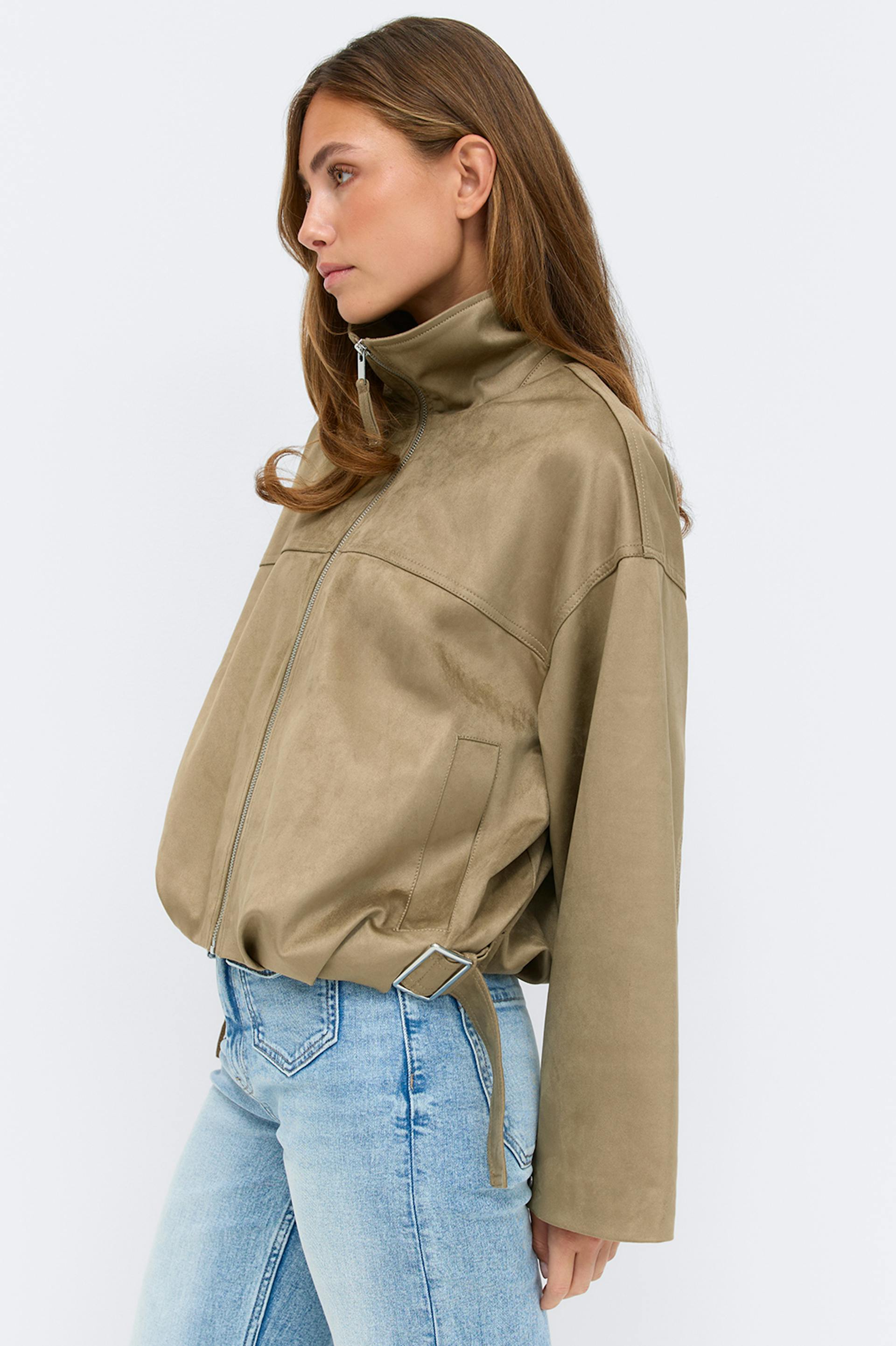 Übergroße braune Wildlederjacke mit Reißverschluss, hohem Stehkragen, Gürtel am Saum und Seitentaschen; große Schildpatt-Sonnenbrille; Jeans in dunkler Waschung.