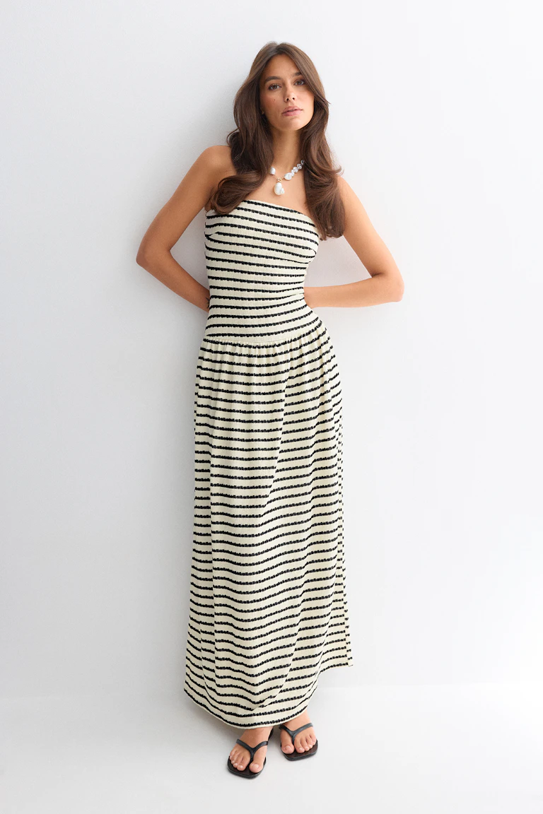 Trägerloses creme-schwarzes, horizontal gestreiftes Maxikleid mit tailliertem, gesmoktem Oberteil, kombiniert mit schwarzen Zehenstegsandalen und einer klobigen Perlenkette.