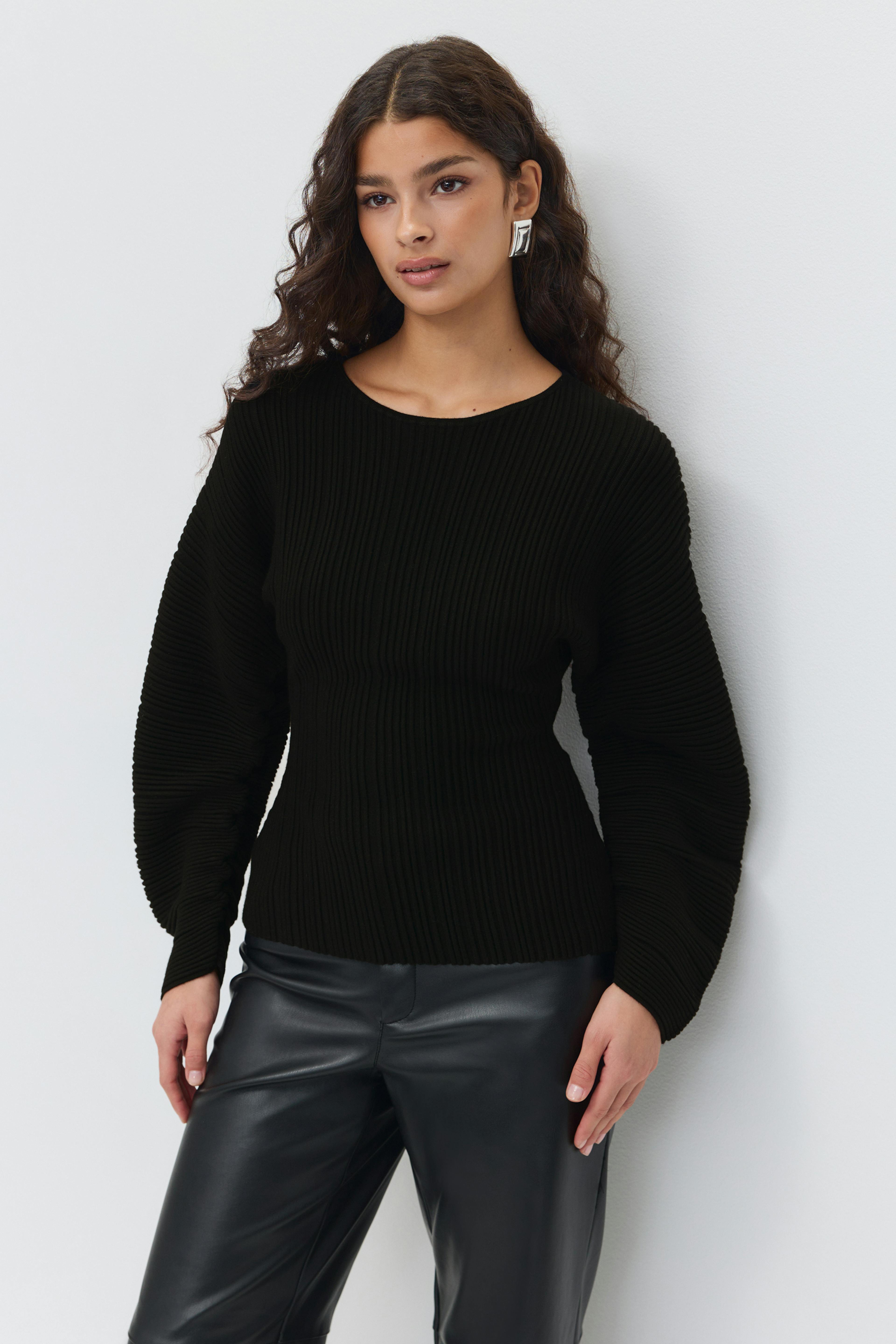 Sort ribstrikket sweater med rund halsudskæring, tætsiddende talje og voluminøse ballonærmer; sorte bukser i læderlook; sølvfarvede geometriske statement-øreringe.