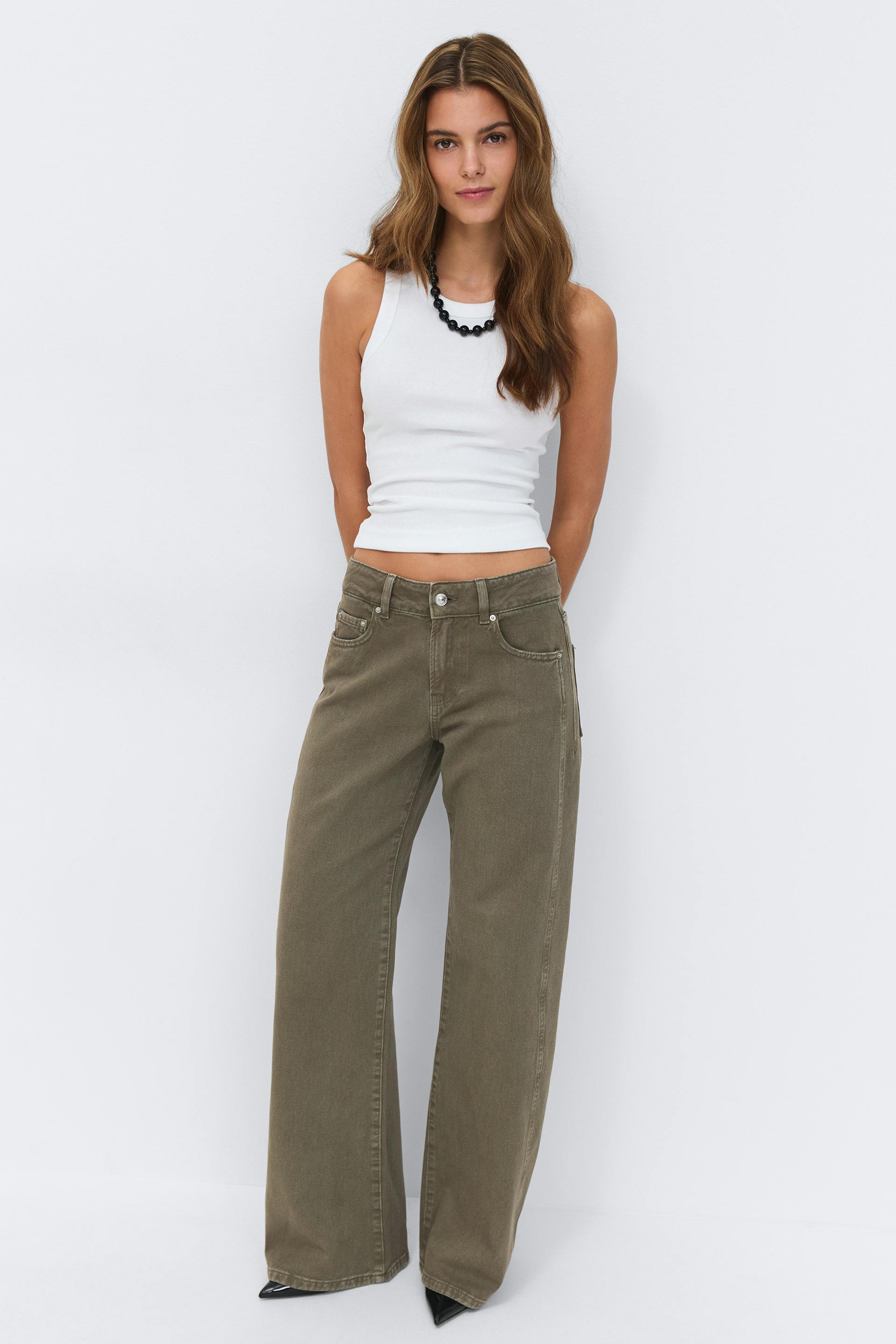 Weißes, geripptes, ärmelloses Tanktop gepaart mit olivgrünen, hochgezogenen Jeans mit weitem Bein, einer schwarzen Perlenkette und schwarzen, spitzen Schuhen.