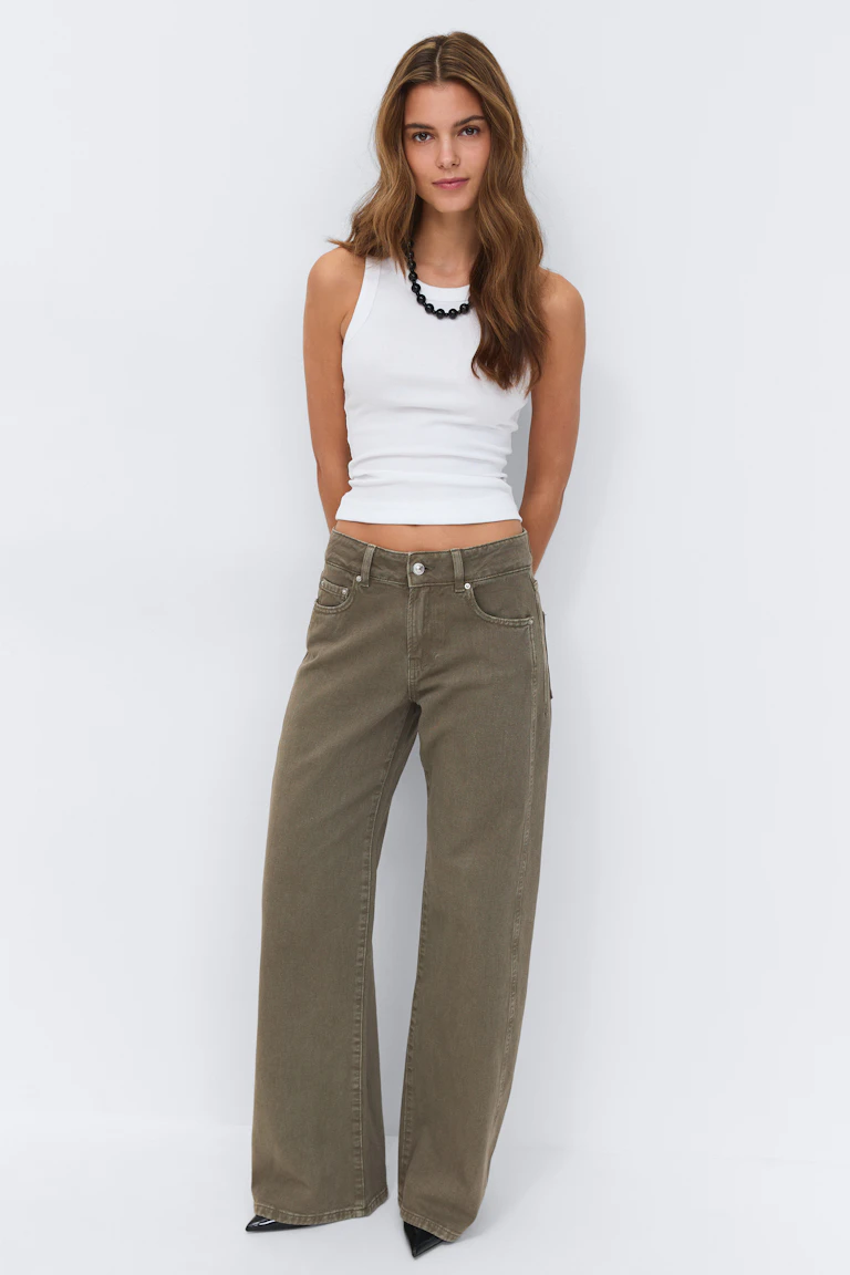 Débardeur blanc sans manches en côtes associé à un jean large à taille haute vert olive, à un collier de perles noires et à des chaussures noires à bout pointu.