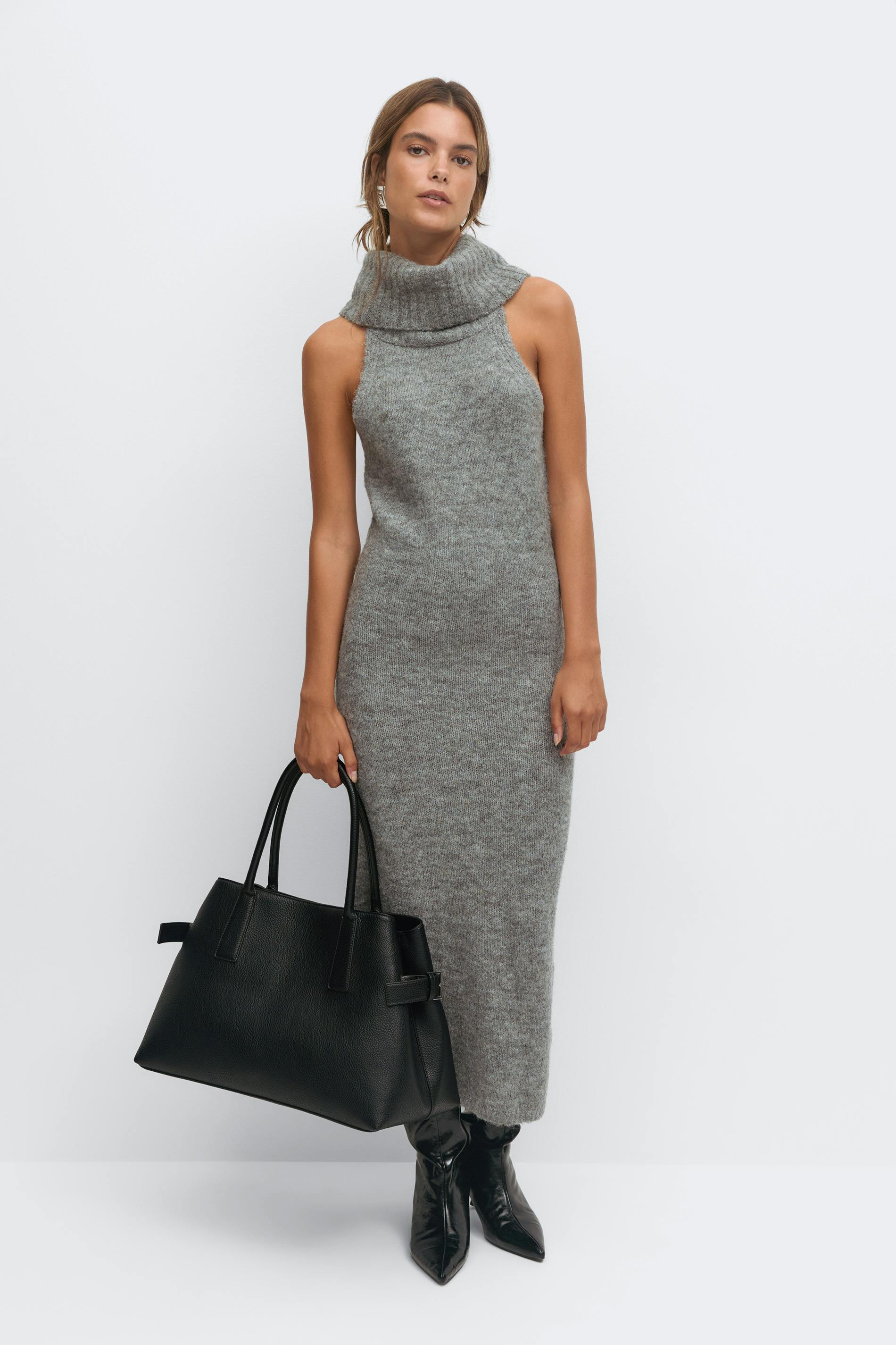 Hihaton harmaa neulottu midi-mekko, jossa on taitettu turtleneck ja joka on yhdistetty mustiin teräväkärkisiin nilkkureihin, suureen mustaan nahkakangaskoteloon ja hopeisiin korvakoruihin.