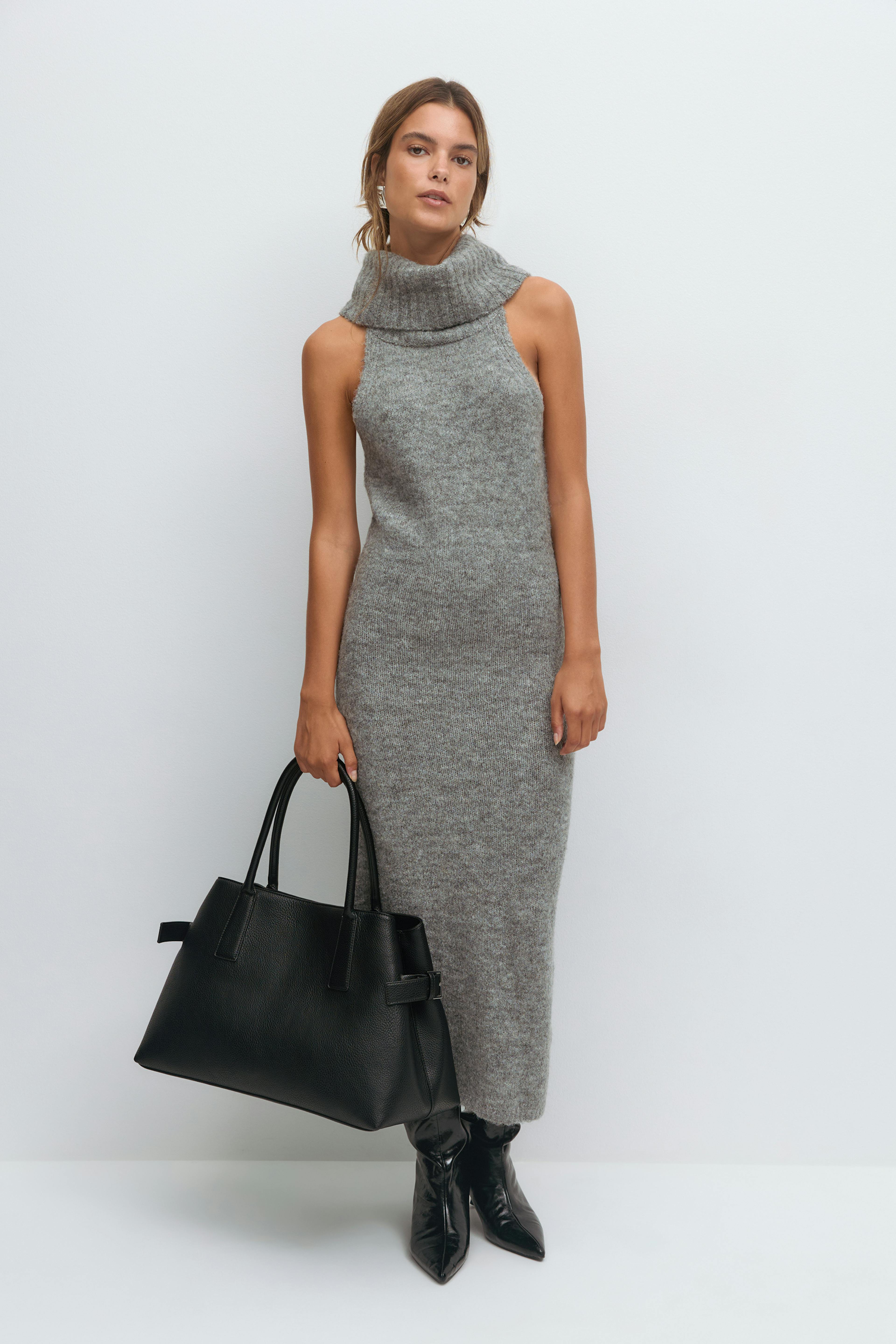 Robe midi sans manches en maille grise avec un col roulé plié, associée à des bottines noires à bouts pointus, un grand fourre-tout en cuir noir et des boucles d'oreilles argentées.