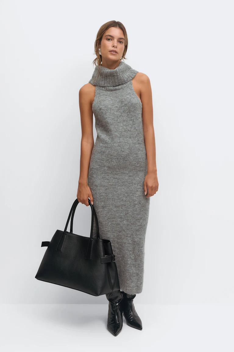 Mouwloze grijze gebreide midi-jurk met een omgeslagen col, gestyled met zwarte enkellaarsjes met spitse teen, een grote zwarte leren tas en zilveren oorbellen.
