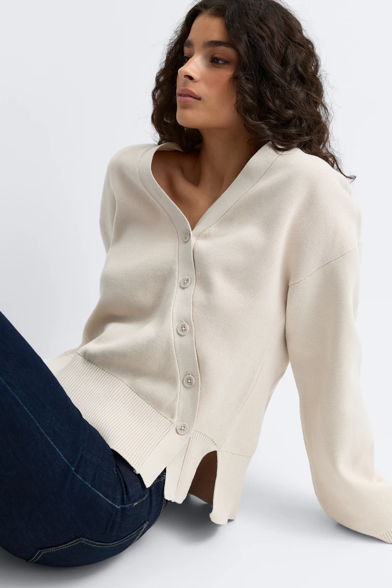 Kremfarget finstrikket cardigan med V-hals og knapp foran, lange ermer, ribbestrikket nederkant og slisser i sidene, stylet med mørke indigofargede jeans i slim fit-modell.