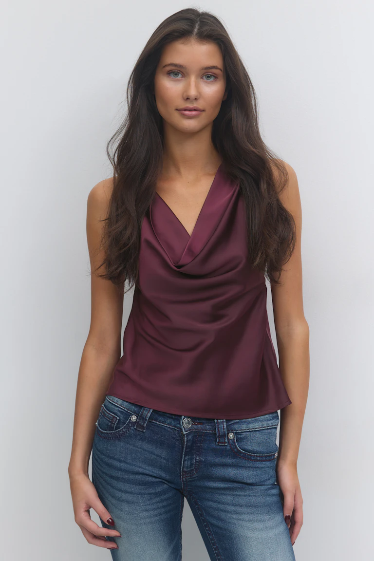 Mouwloze bordeauxrode satijnen blouse met cowl-hals in combinatie met een blauwe jeans met middelhoge taille.