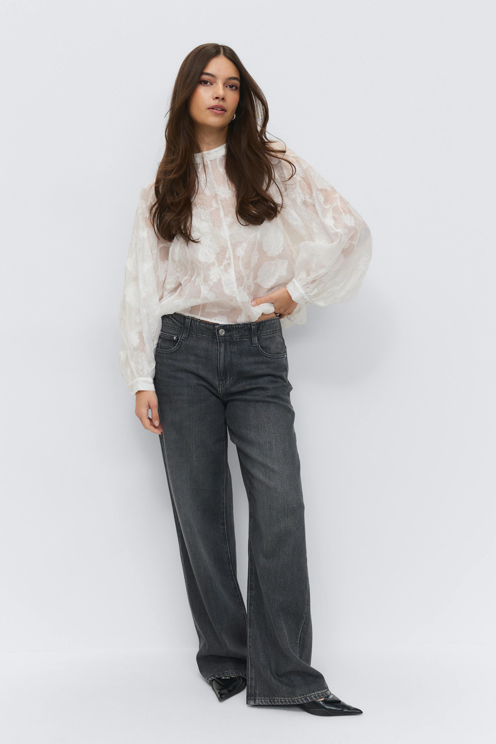 White sheer floral jacquard long-sleeve blouse with high neckline and voluminous sleeves; faded black high‑waisted wide‑leg jeans; black pointed‑toe leather pumps.