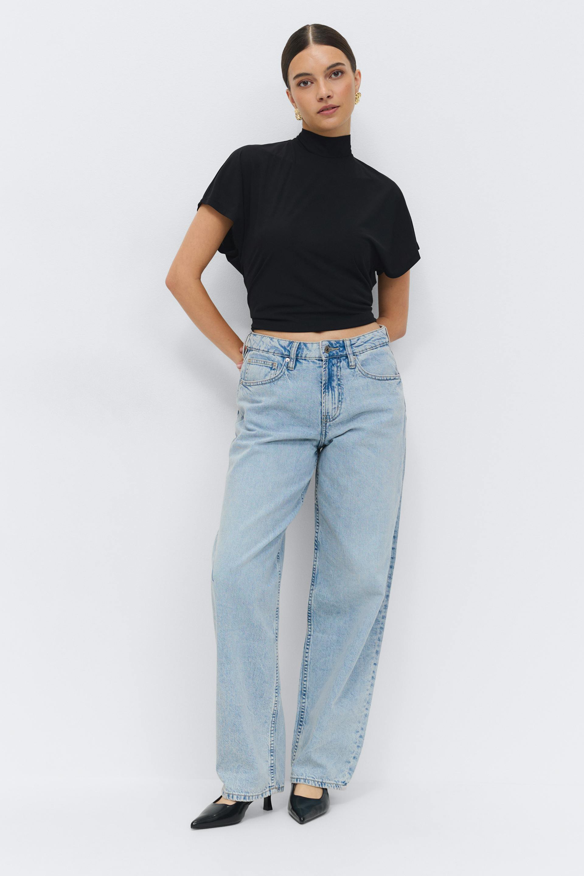 Black short-sleeve mock-neck cropped top paired with light-wash high-rise wide-leg jeans and black pointed-toe heeled pumps, accessorized with gold statement earrings.
