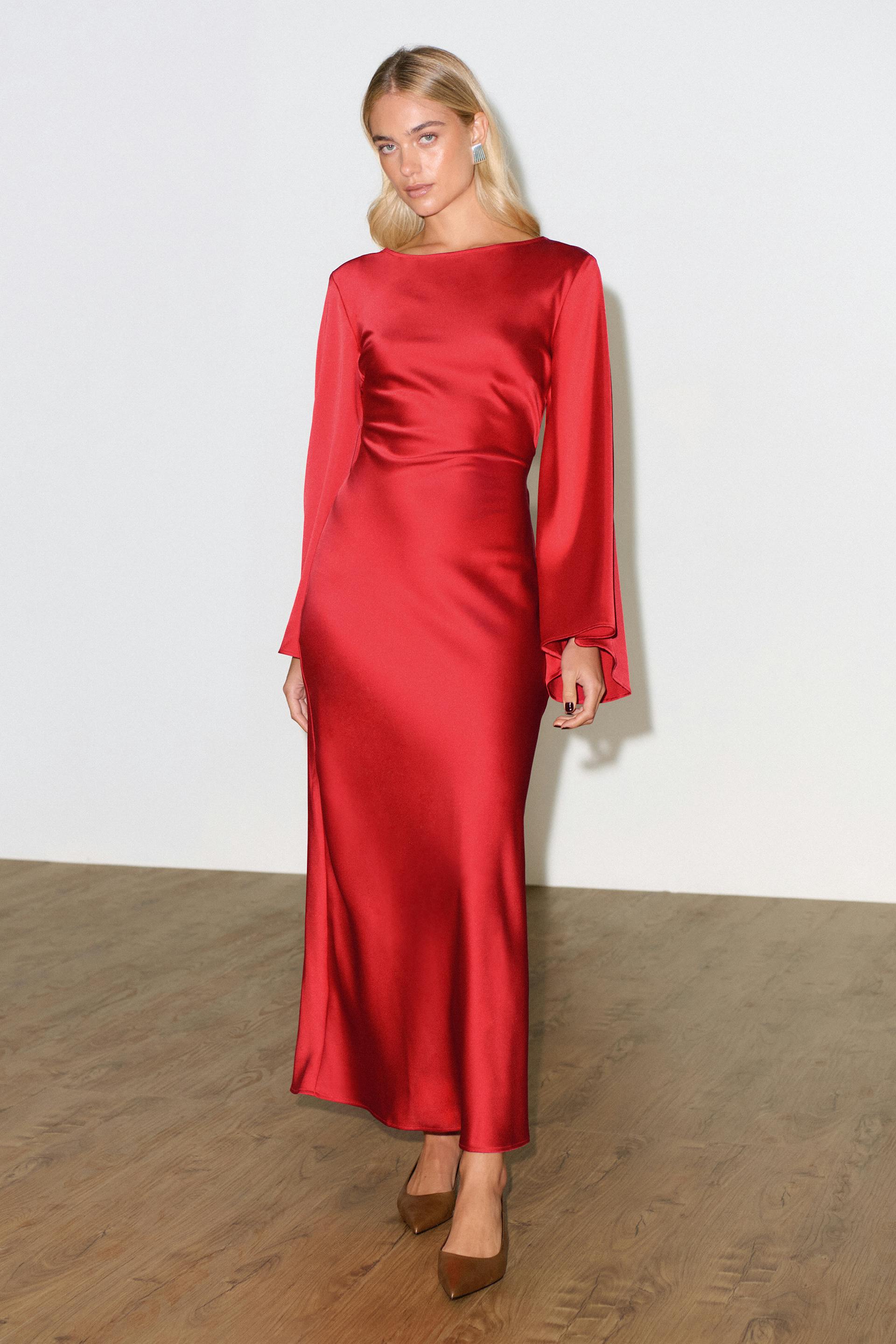 Red satin, long-sleeve floor-length gown with a boat neckline and fitted waist, paired with brown pointed-toe heels and silver rectangular earrings.