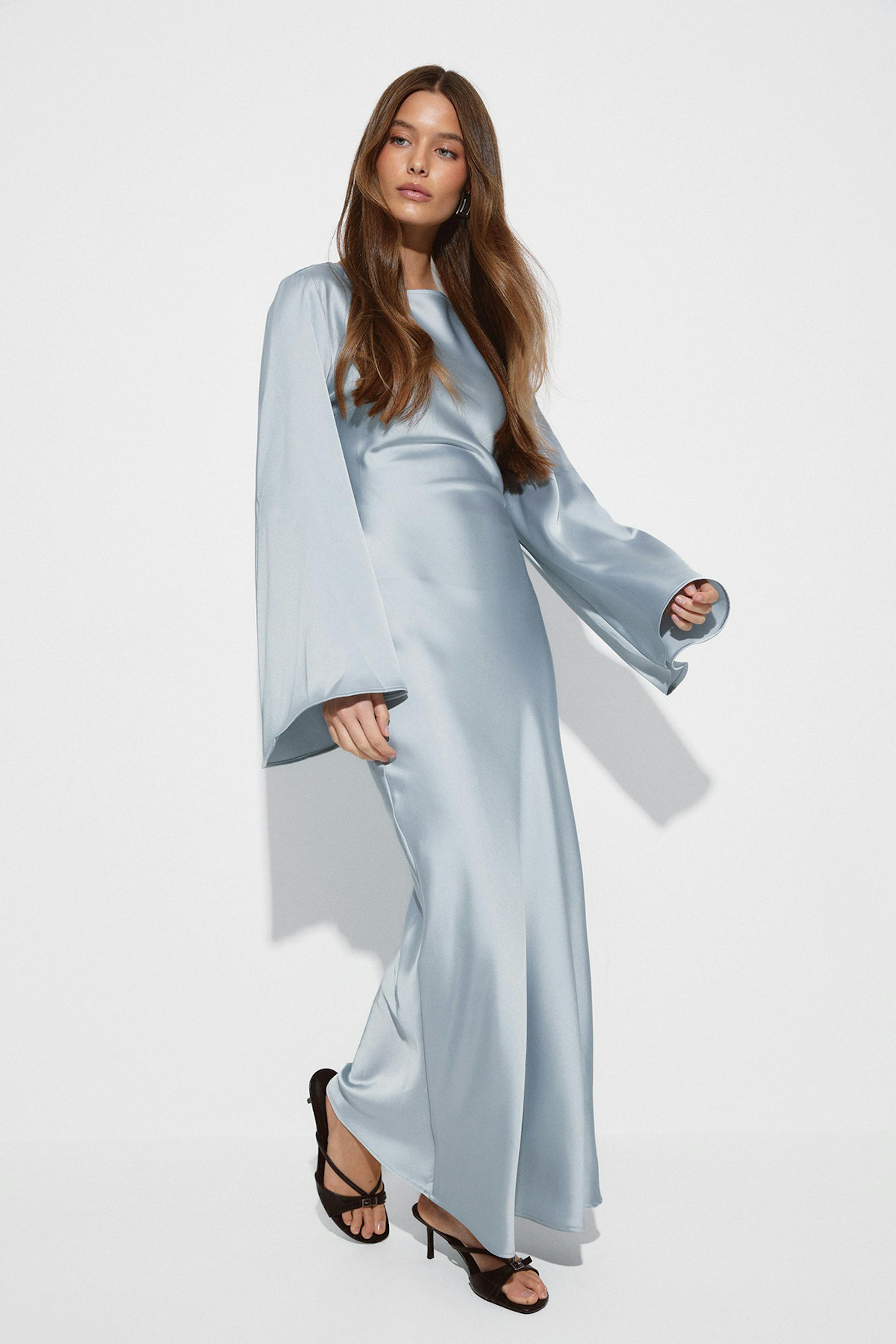 Robe longue en satin bleu pâle à encolure ronde et manches cloche surdimensionnées, associée à des sandales noires à talons hauts.