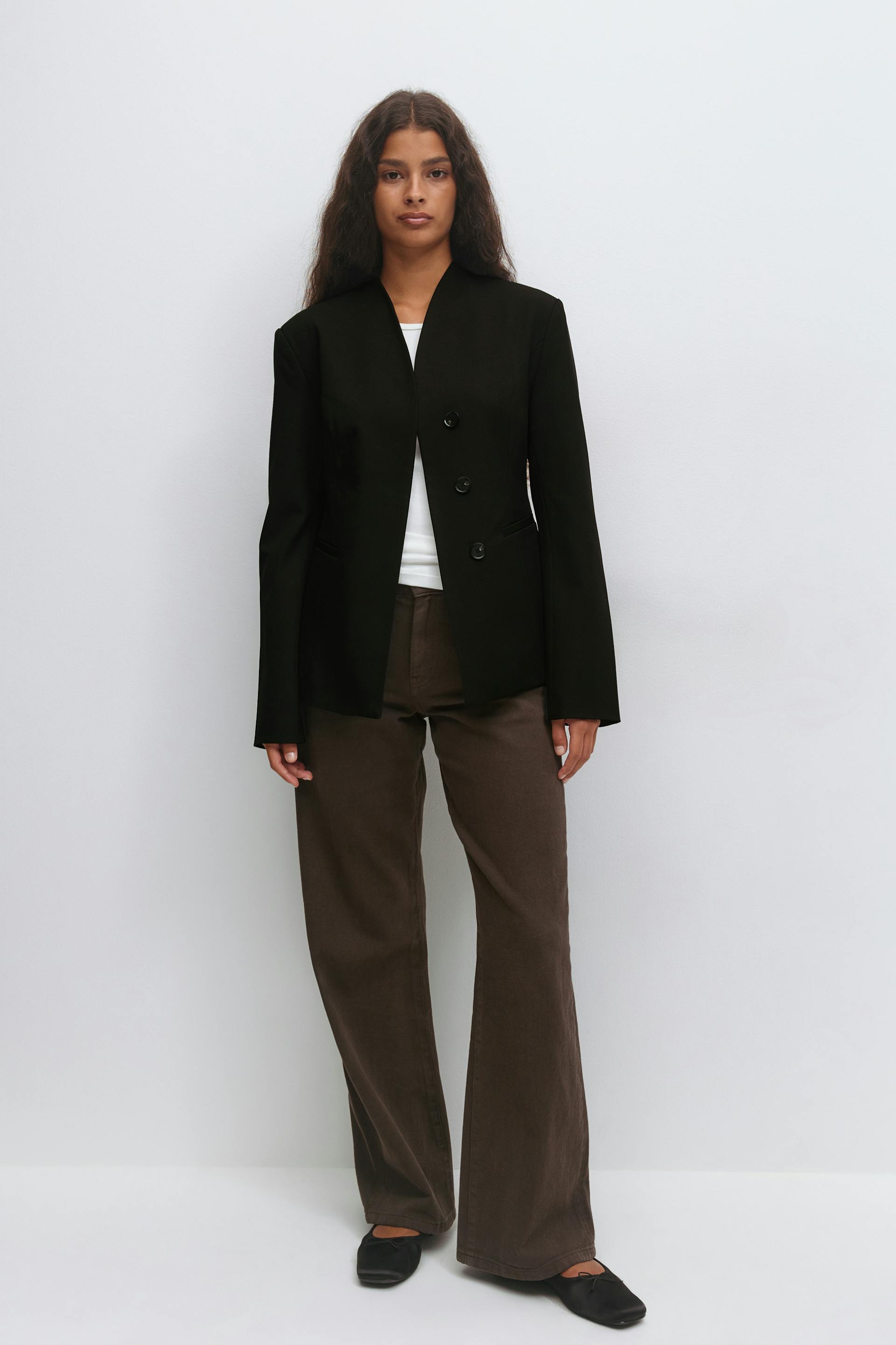 Black structured three-button blazer over a white crew-neck top, paired with brown wide-leg trousers and black ballet flats.