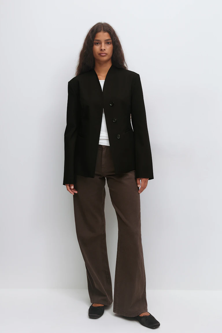 Blazer noir structuré à trois boutons sur un top blanc à col ras du cou, associé à un pantalon large marron et à des ballerines noires.
