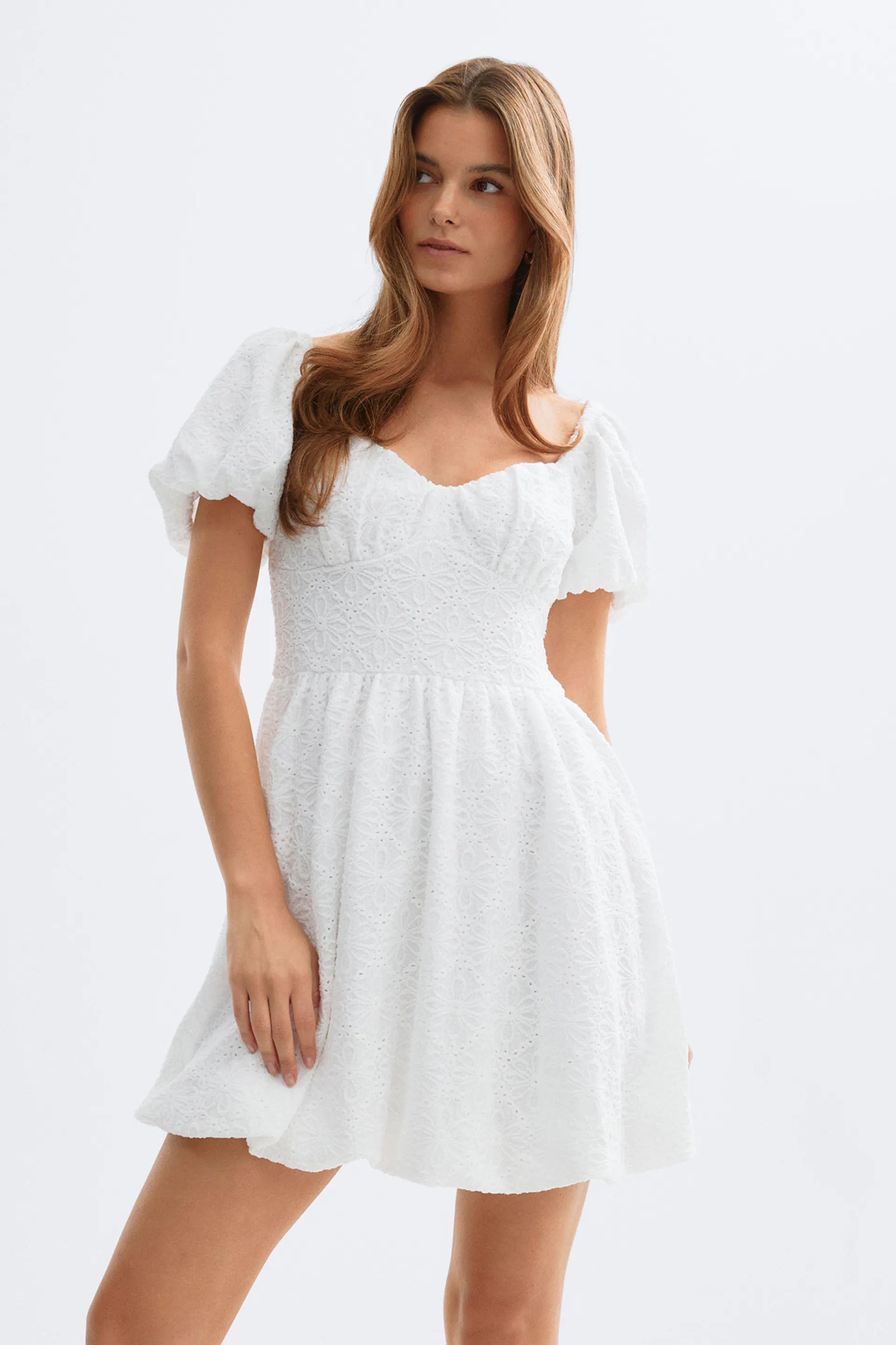 Hvid minikjole i broderie anglaise med hjerteudskæring, tætsiddende overdel, korte pufærmer, høj talje og udslået skørt med skulpterede kanter.