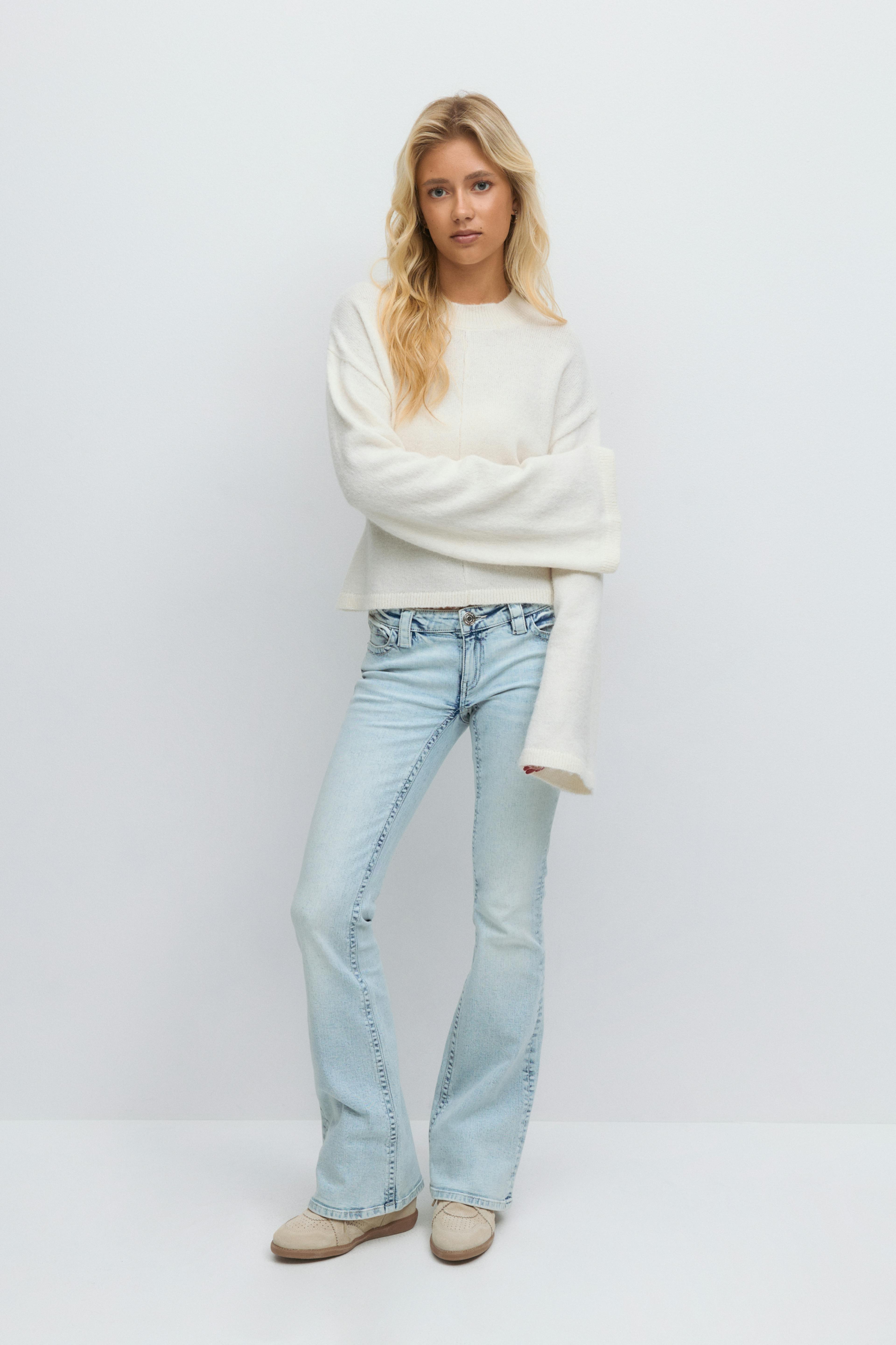 Overdimensjonert strikkegenser med kremfarget rund hals og forlengede ermer, lyse jeans med vidde og beige brogue-sko i semsket skinn.