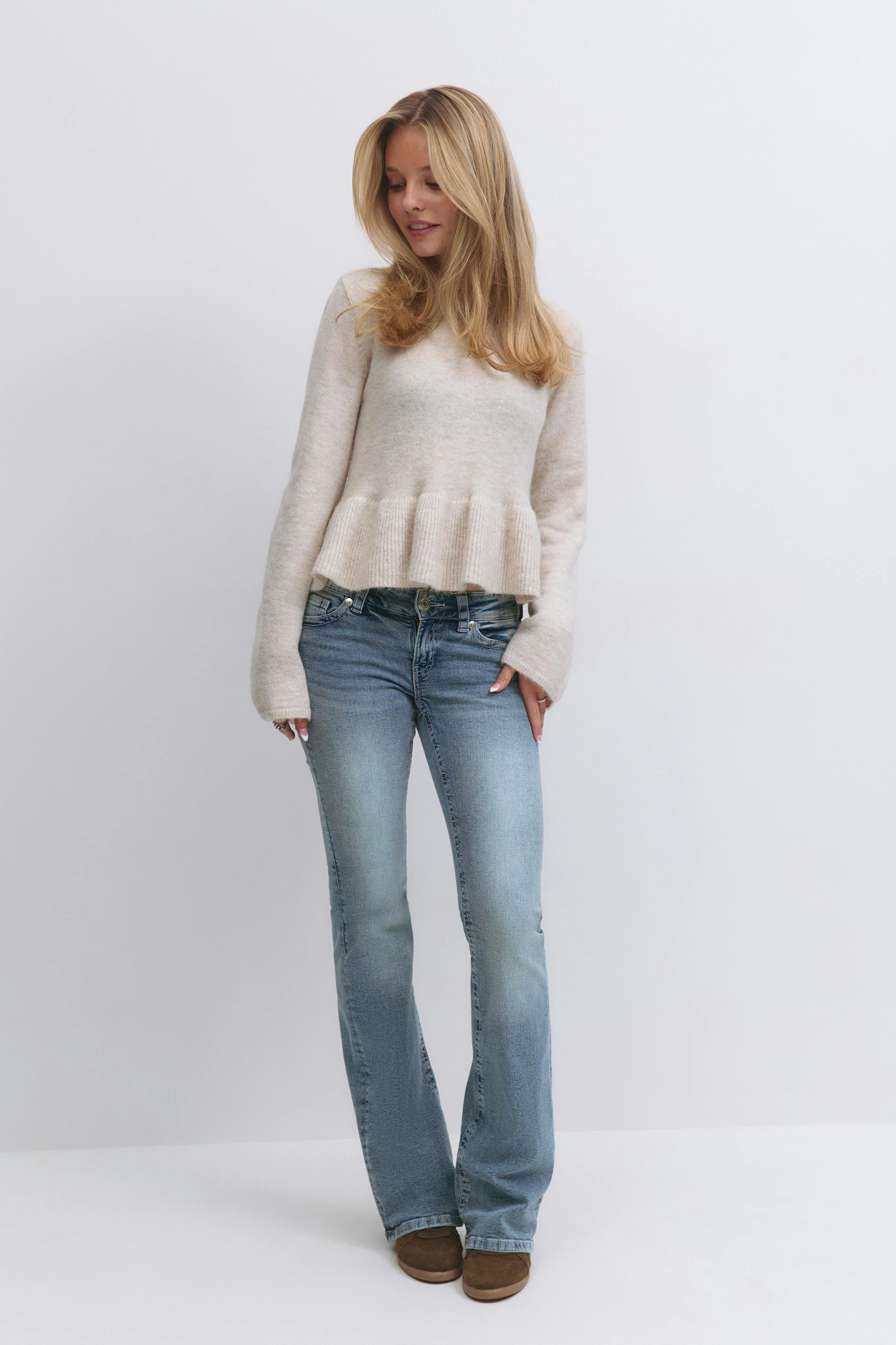 Cream crewneck peplum sweater with long sleeves, light-wash bootcut jeans, and brown suede slip-on shoes.