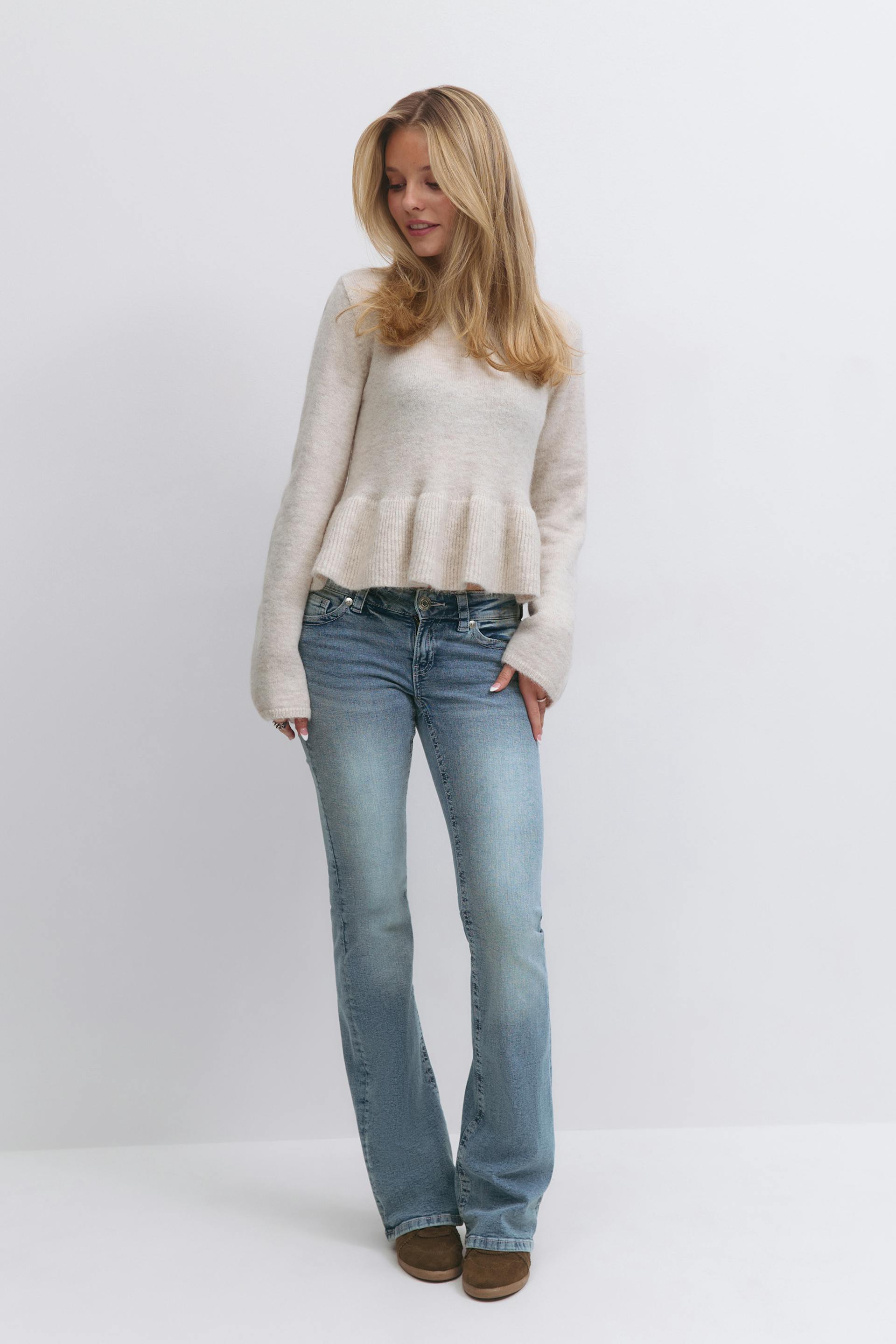 Cream crewneck peplum sweater with long sleeves, light-wash bootcut jeans, and brown suede slip-on shoes.
