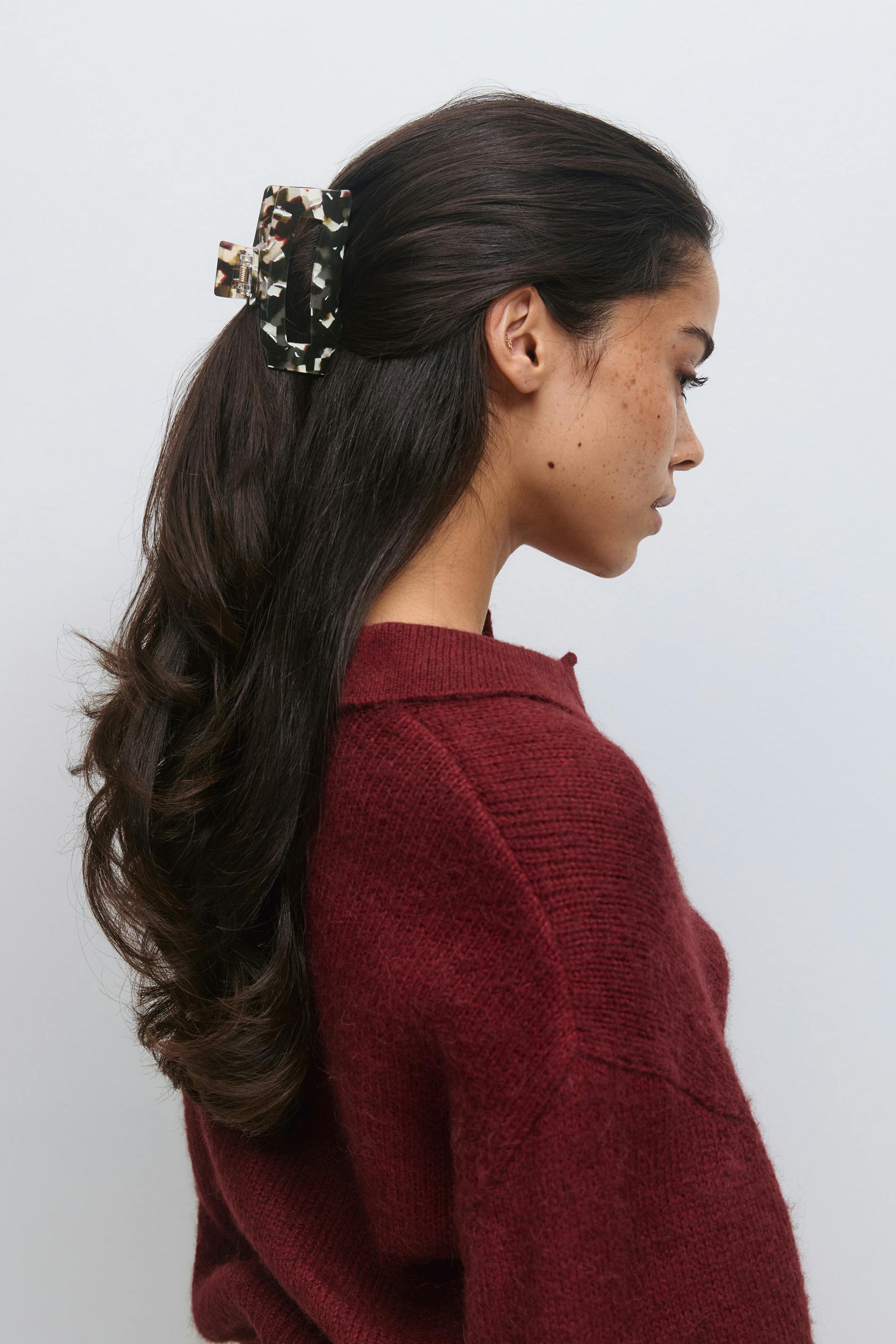 Pull en maille texturée bordeaux foncé avec un petit col et une pince à cheveux rectangulaire marbrée noir et crème.