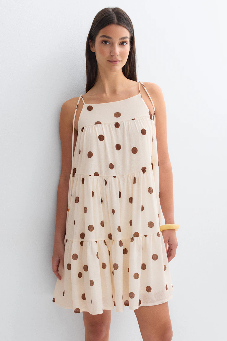 Cremefarbenes, gestuftes Minikleid mit braunen Tupfen, quadratischem Ausschnitt und Spaghettiträgern zum Binden, kombiniert mit einem gelben Armreif.