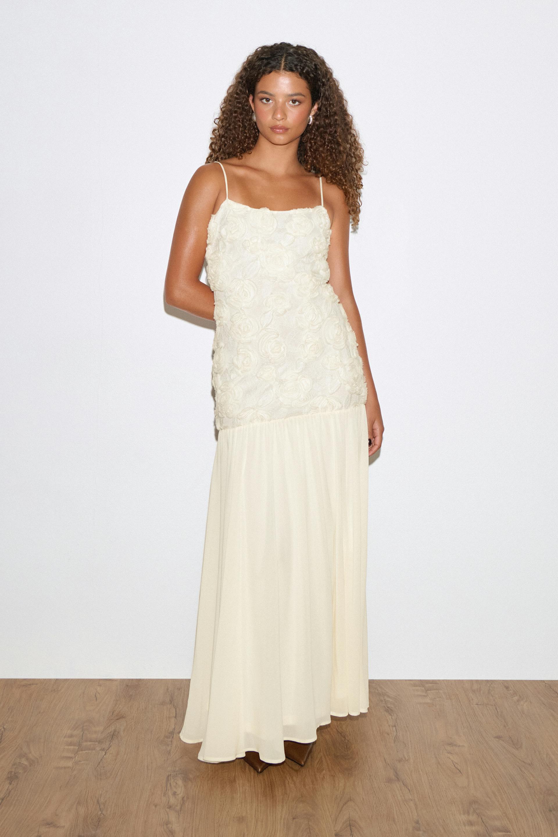 Ivory floor-length gown with thin spaghetti straps, a fitted bodice covered in three-dimensional rose appliqués and a flowing chiffon skirt.