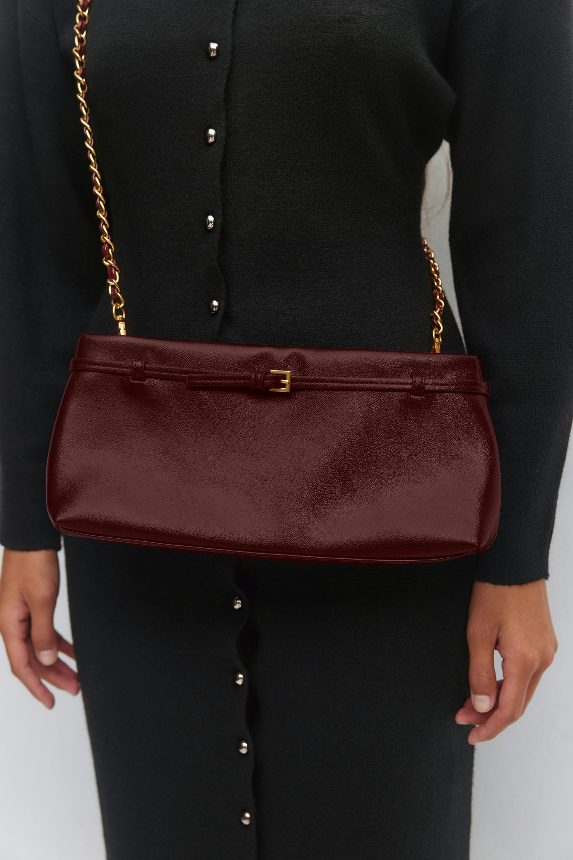 Black long-sleeve button-front knit dress with silver buttons, paired with a burgundy leather shoulder bag featuring a gold chain strap and small buckle detail.