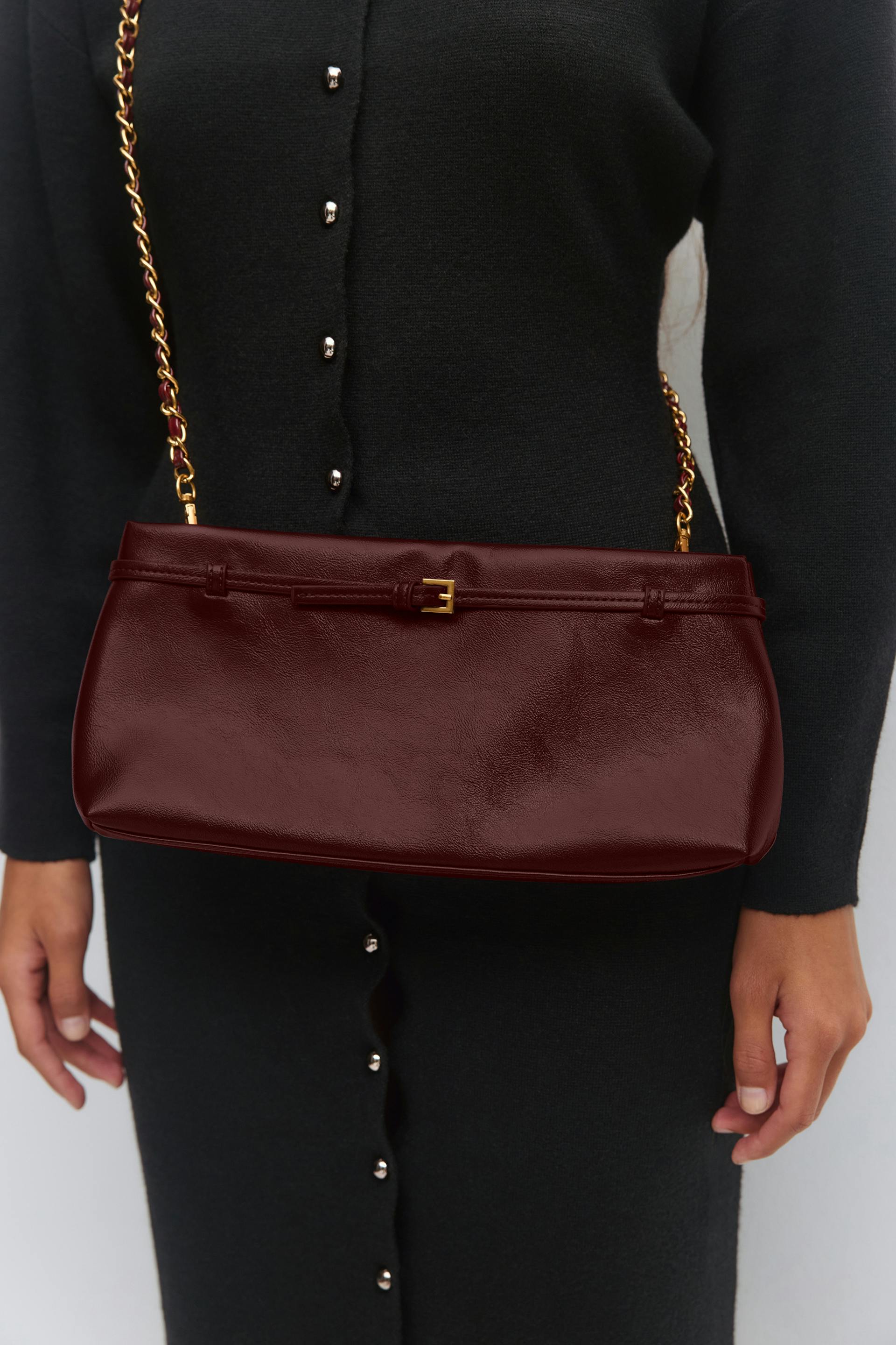 Black long-sleeve button-front knit dress with silver buttons, paired with a burgundy leather shoulder bag featuring a gold chain strap and small buckle detail.