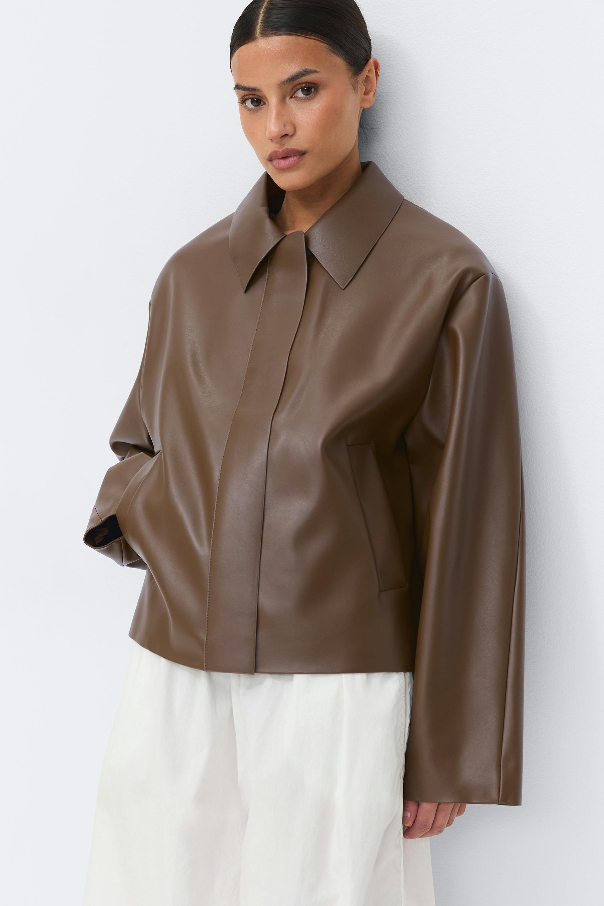 Brown leather-look collared jacket with concealed front placket, side welt pockets and long sleeves, paired with loose white wide-leg trousers.