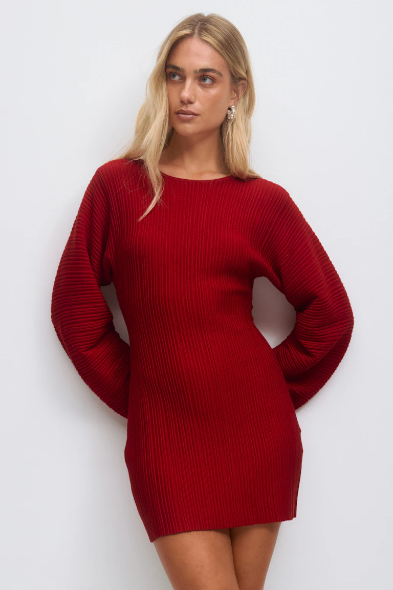 Rotes Minipullover-Kleid aus Rippstrick mit langen, voluminösen Ärmeln und Rundhalsausschnitt, gestylt mit silbernen Statement-Ohrringen.