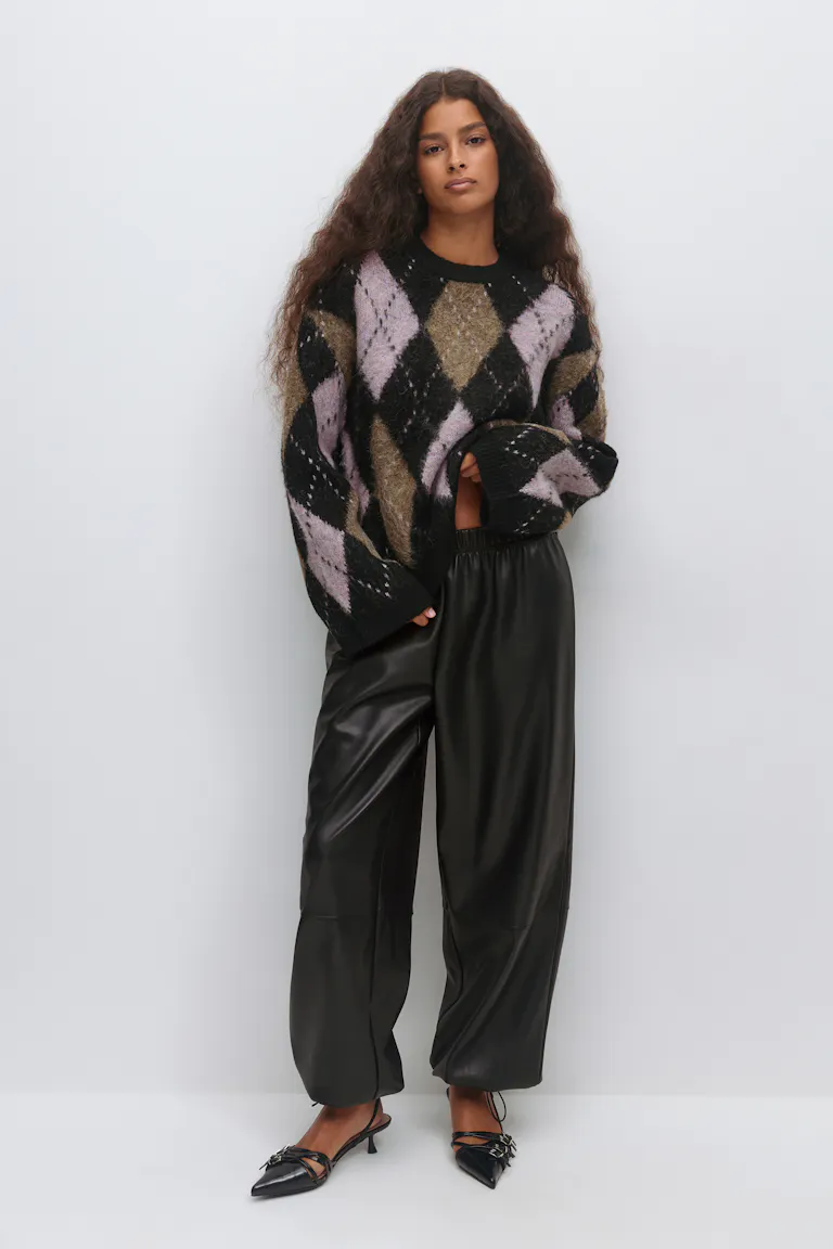 Oversized fuzzy argyle sweater i sort, lilla og oliven, sorte bukser med brede ben i kunstlæder med elastisk linning og sorte spidse slingback-sko med kitten-heel og remdetaljer.