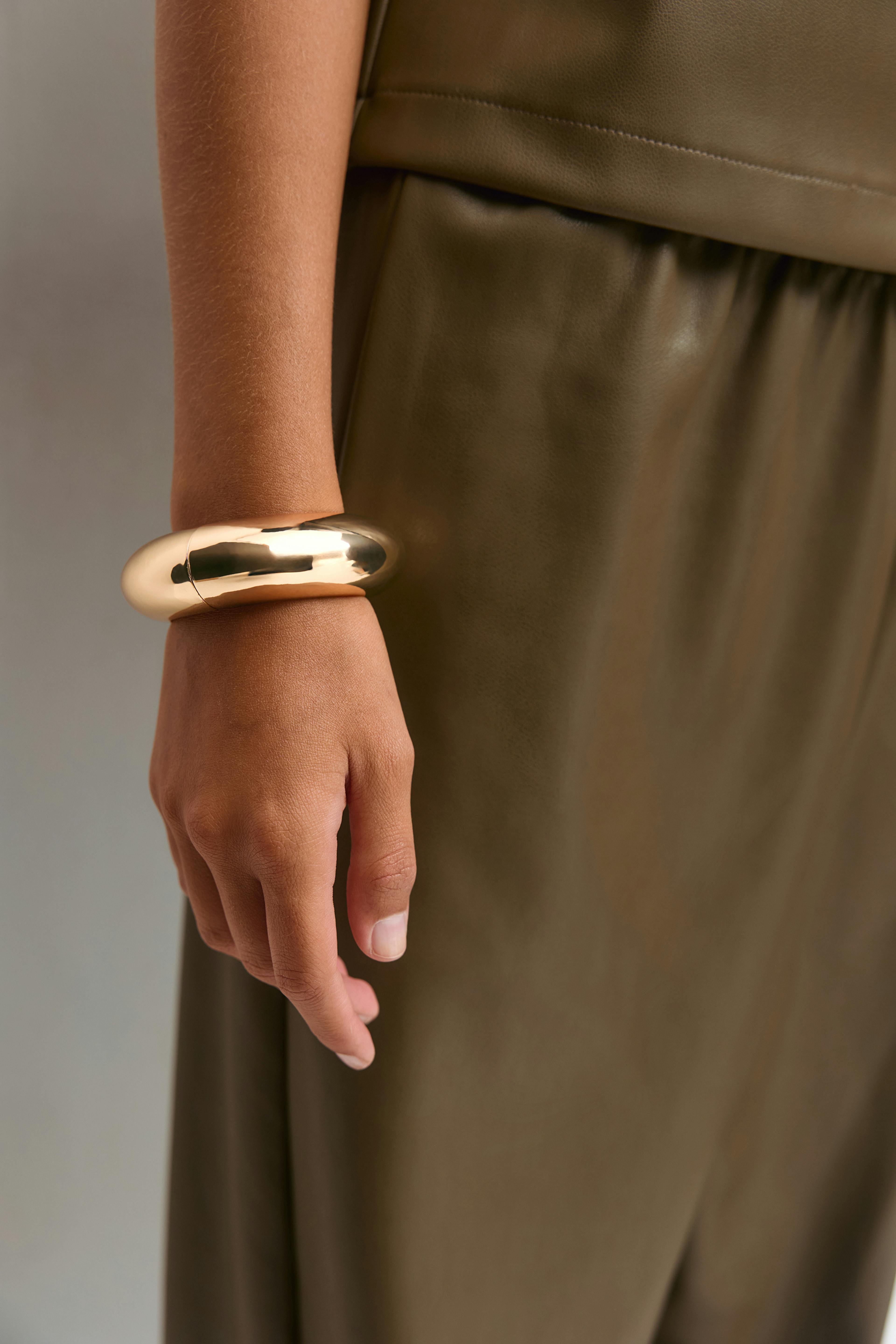 Olive-green leather-look sleeveless top and matching skirt, paired with an oversized polished gold cuff bracelet.