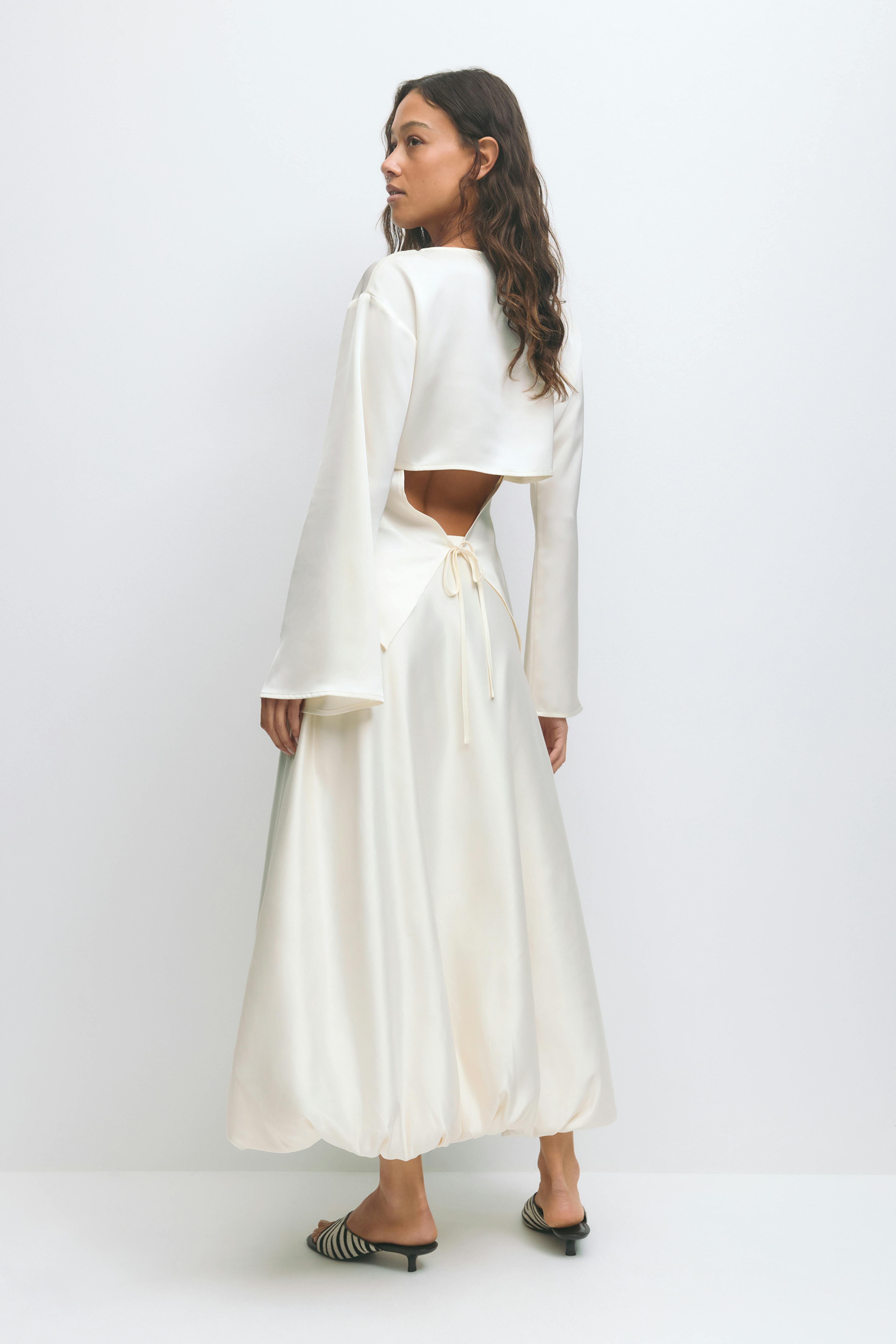 Elfenbensfarvet satinsæt: langærmet top med vide ærmer og åben ryg, der bindes i taljen, parret med en højtaljet, ankellang nederdel med rynket ballonkant; zebrastribede lavhælede muldyr.