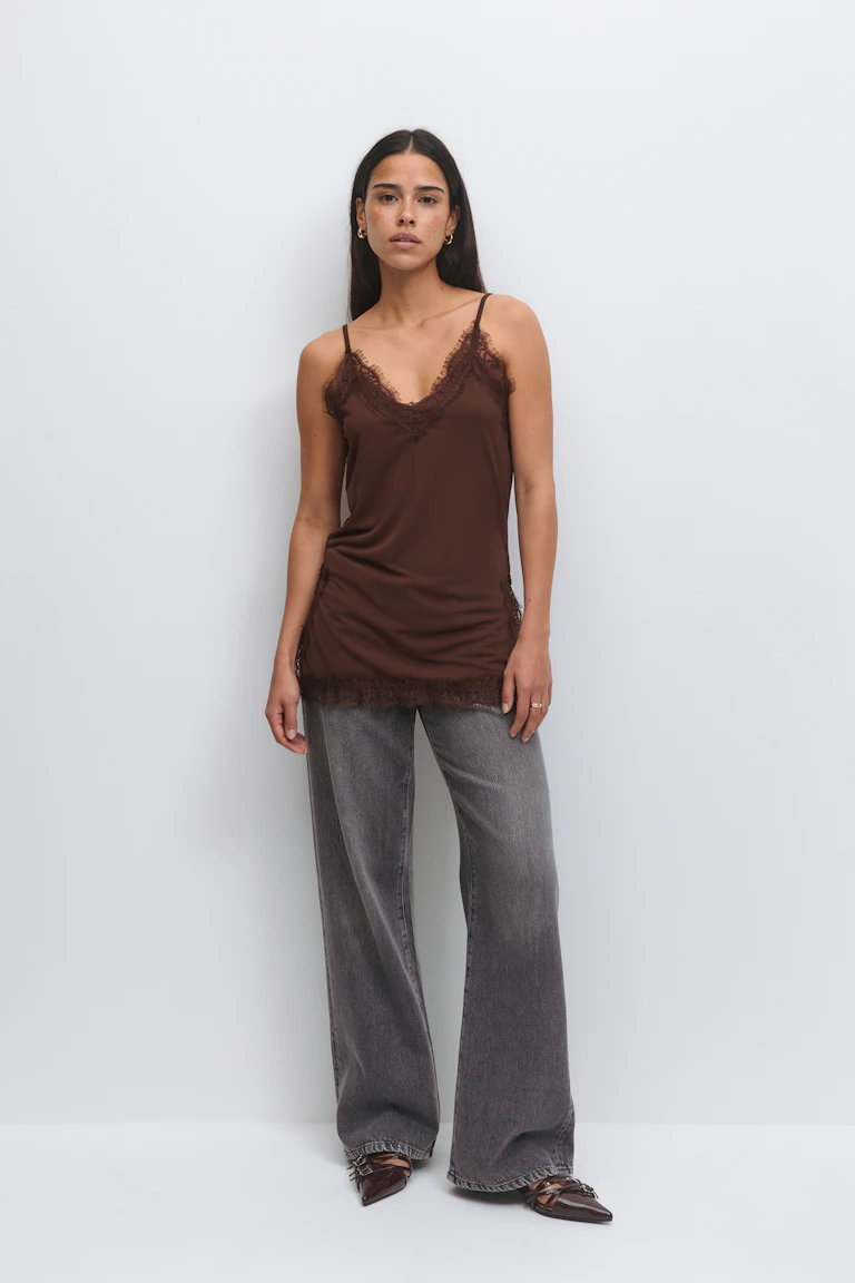 Caraco en satin marron bordé de dentelle avec fines bretelles spaghetti, associé à un jean large gris délavé et à des chaussures plates pointues en cuir marron avec lanières et chaînes.