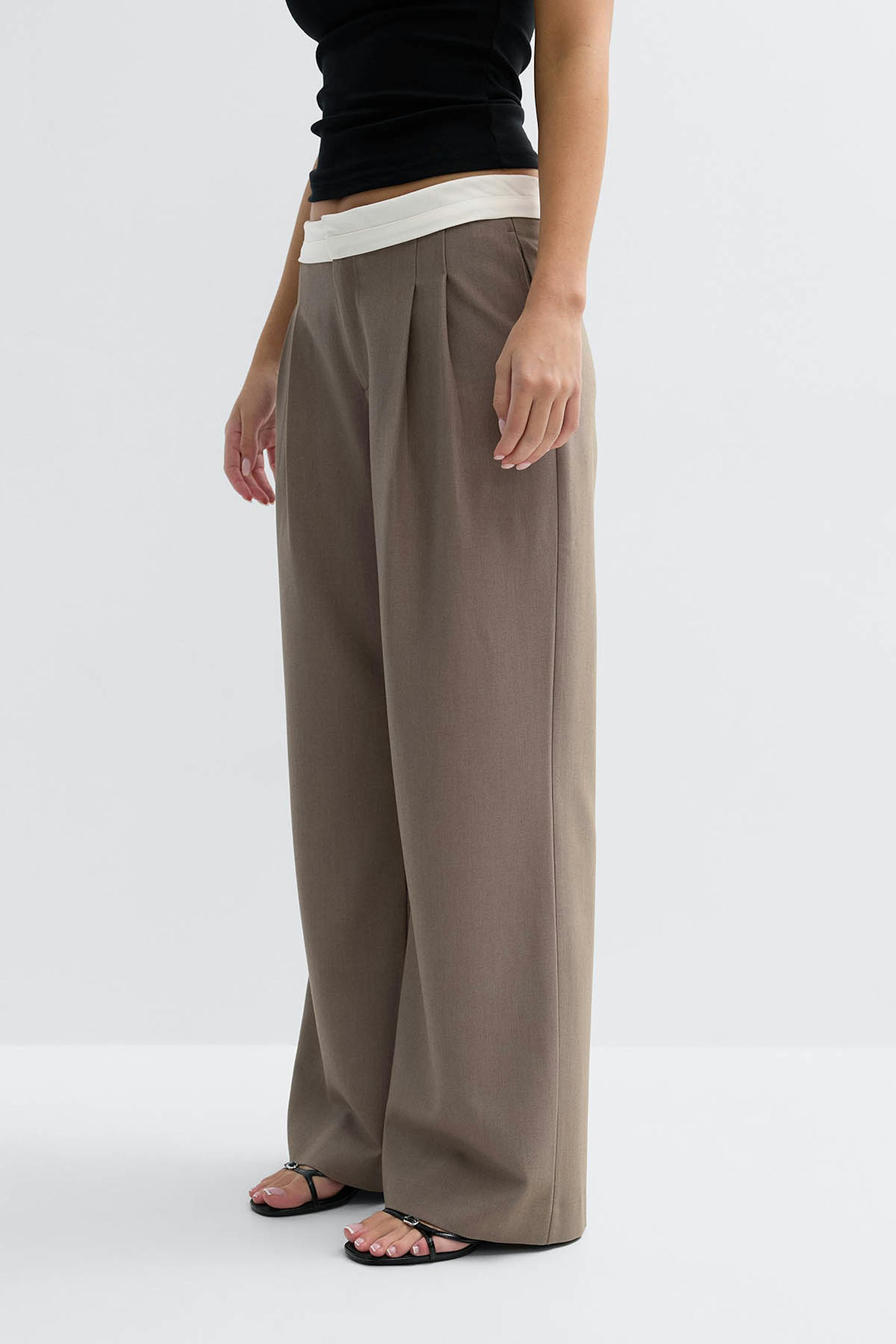 Black sleeveless cropped top paired with high-waisted taupe wide-leg trousers featuring front pleats and a folded white waistband; finished with black strappy flat sandals.