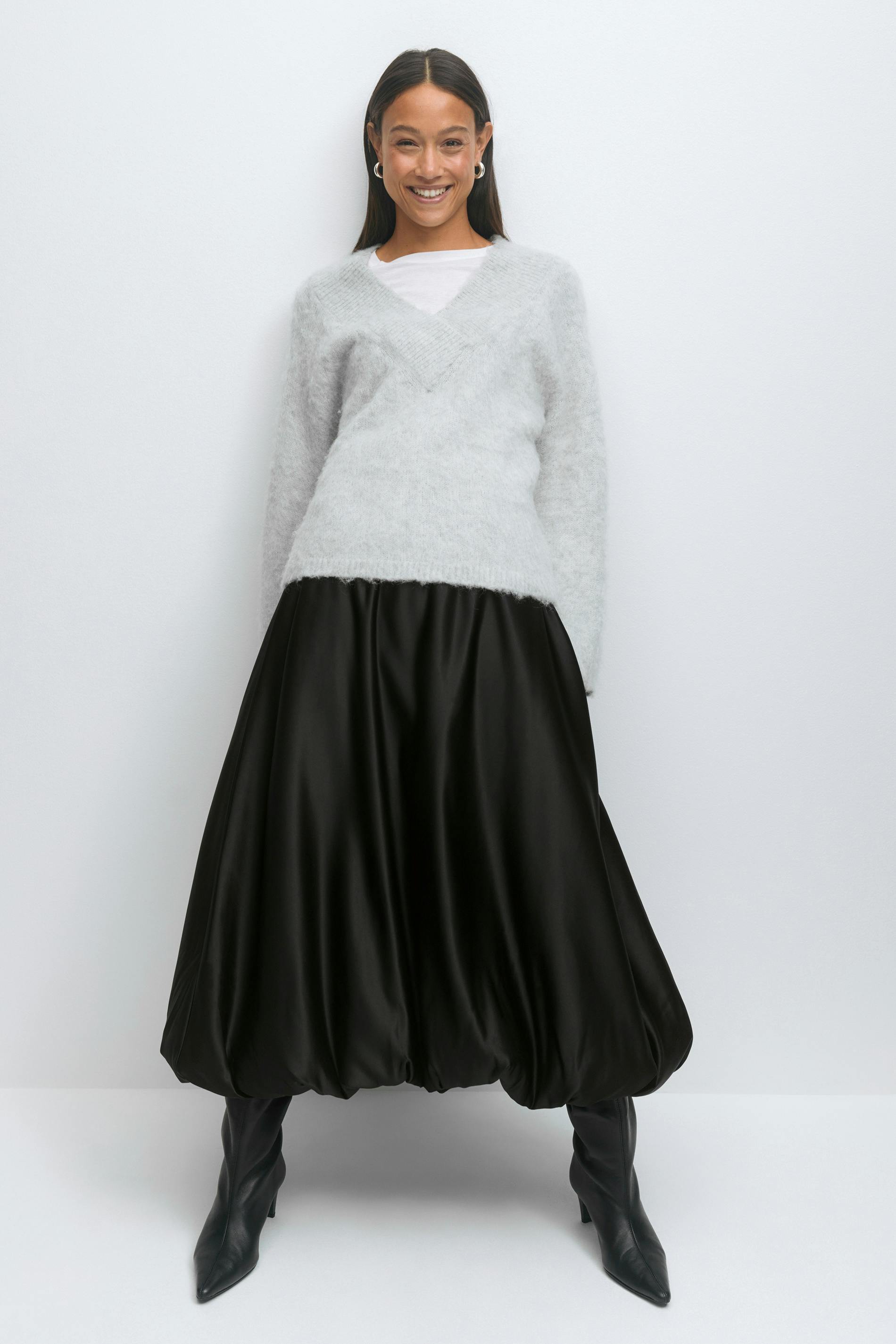 Light grey fuzzy V‑neck sweater layered over a white crew‑neck tee, paired with a black satin voluminous balloon‑hem midi skirt and black pointed‑toe knee‑high boots.