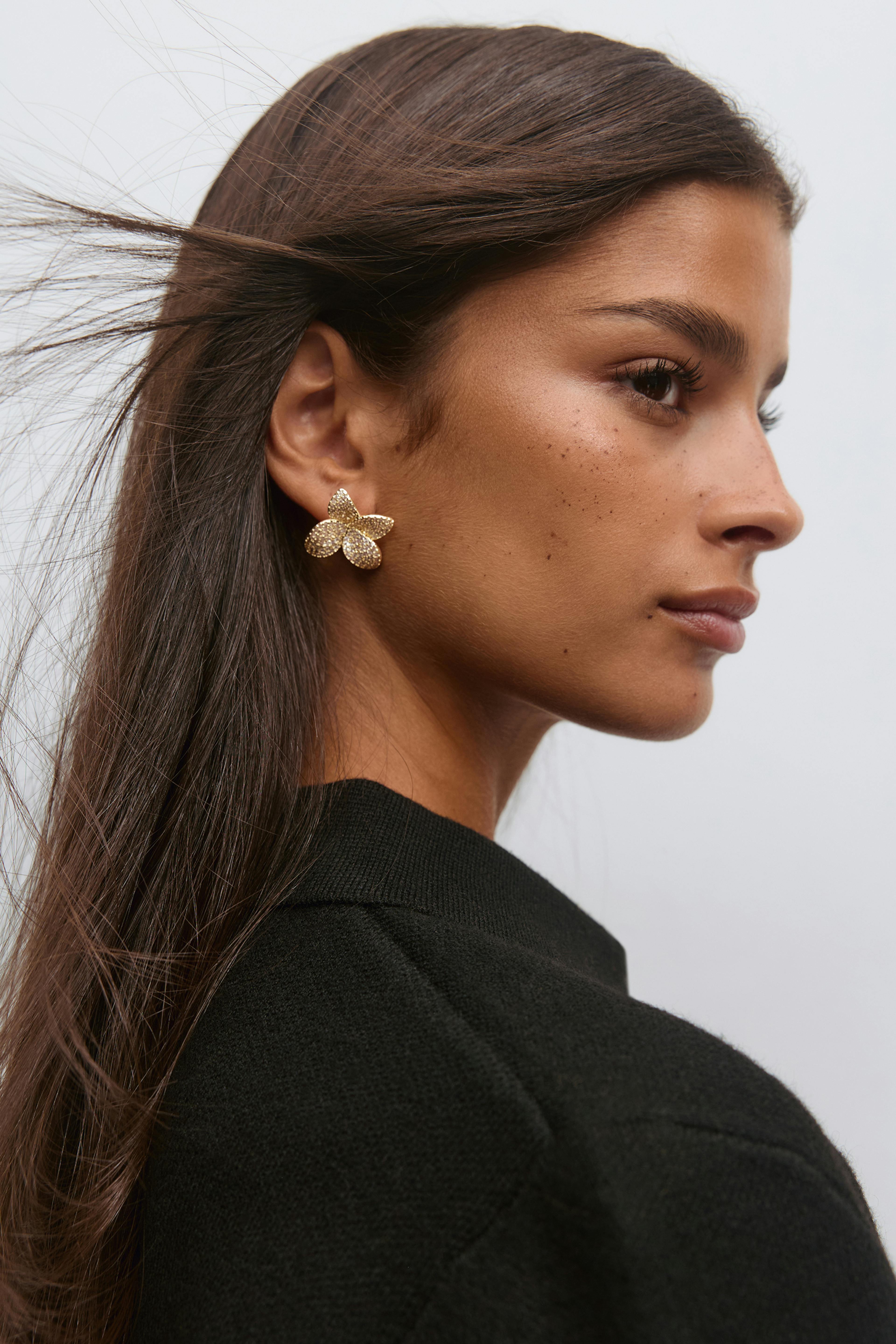 Black crew-neck knit sweater paired with gold textured floral stud earrings.