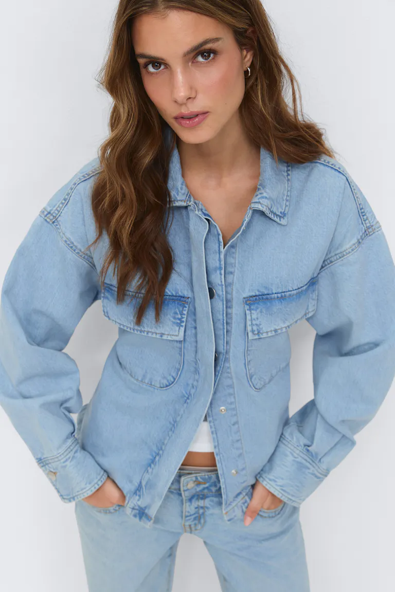 Lys denimjakke med brystlommer med klaff og trykknapper foran, som bæres over en hvit, kort topp og sammen med matchende, lyse denimjeans.
