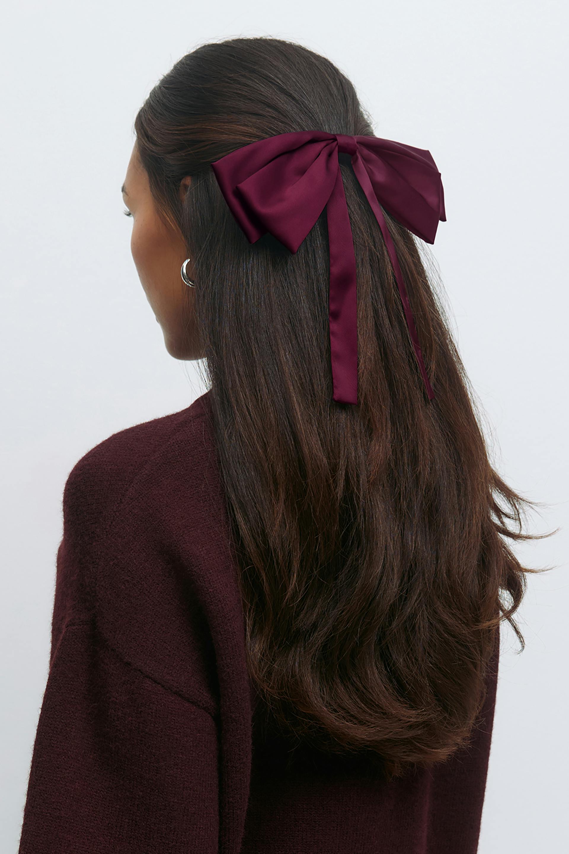 Burgundy knit sweater, silver hoop earrings, and a large burgundy satin bow hair accessory with long trailing ribbons.