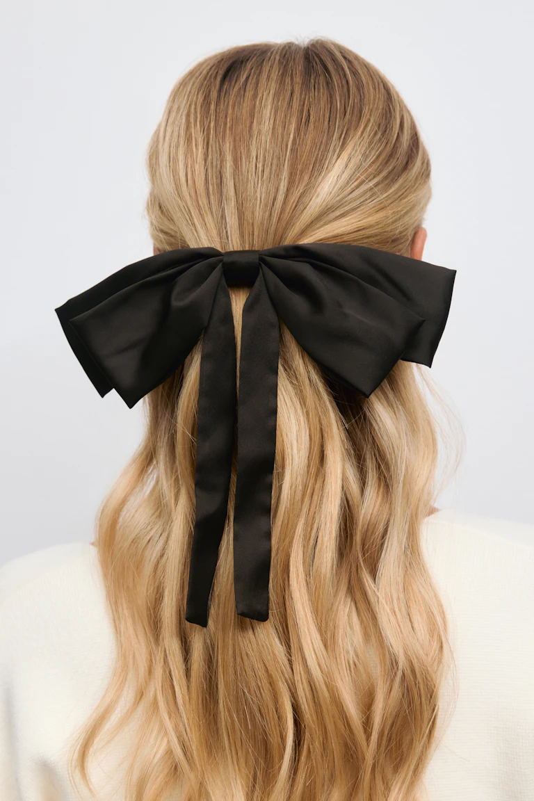 Zwart satijnen oversized strik haaraccessoire voor een half opgestoken stijl, gecombineerd met een crèmekleurige gebreide top.